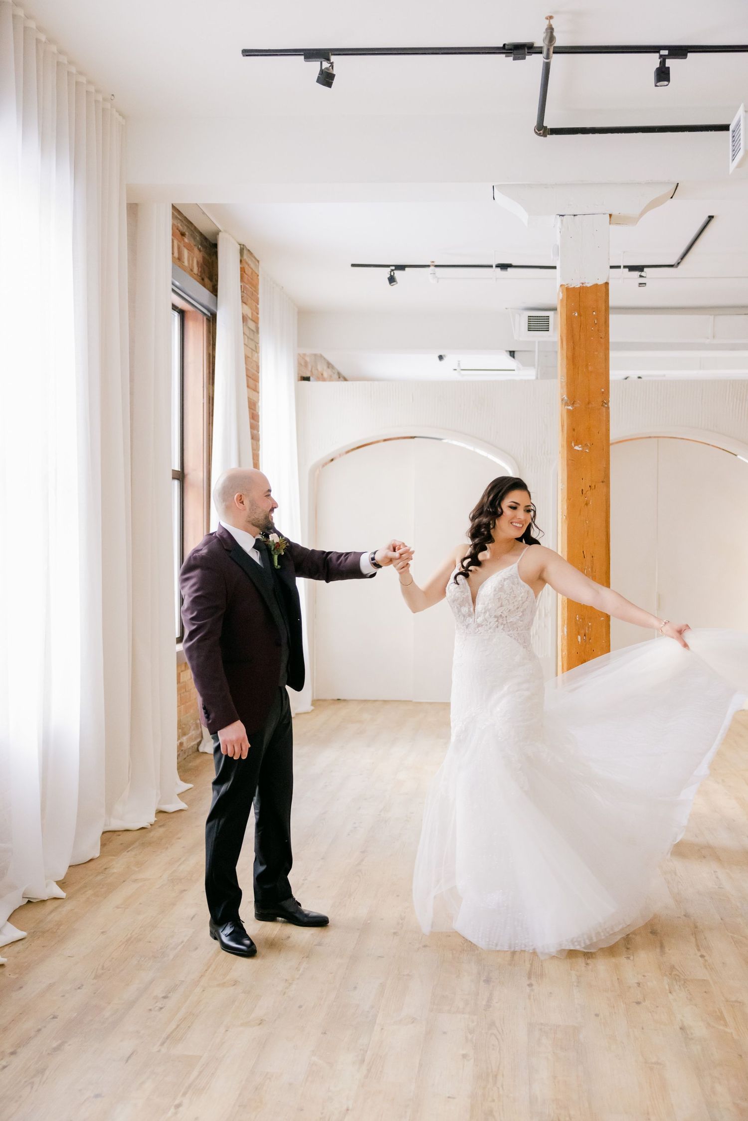 A couple dancing gracefully in an airy venue with wooden pillars and track lighting.