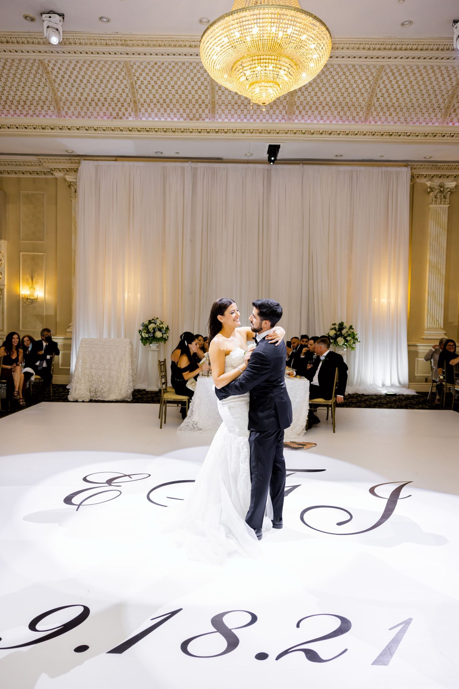 A couple dances under an ornate chandelier on a personalized dance floor with wedding date displayed.