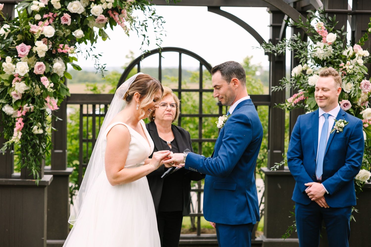 Wedding ceremony moment under pergola decorated with pink roses and white flowers.