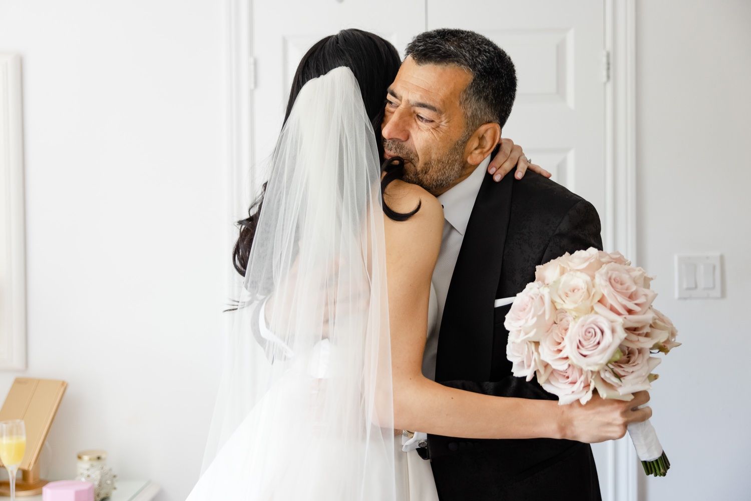 Emotional wedding day embrace with pink rose bouquet.
