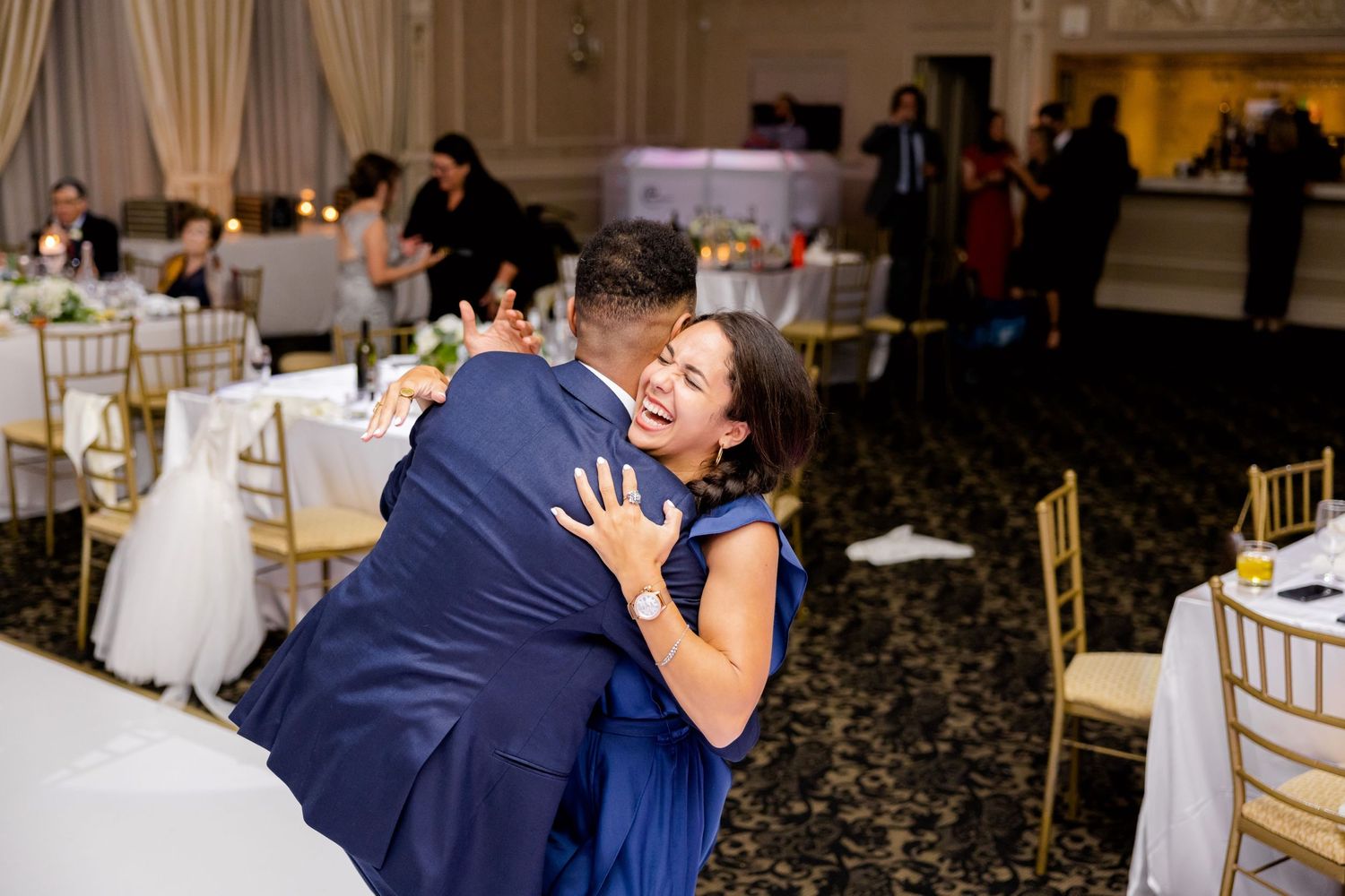 Couple sharing a romantic dance moment in an elegant reception hall with gold chairs.
