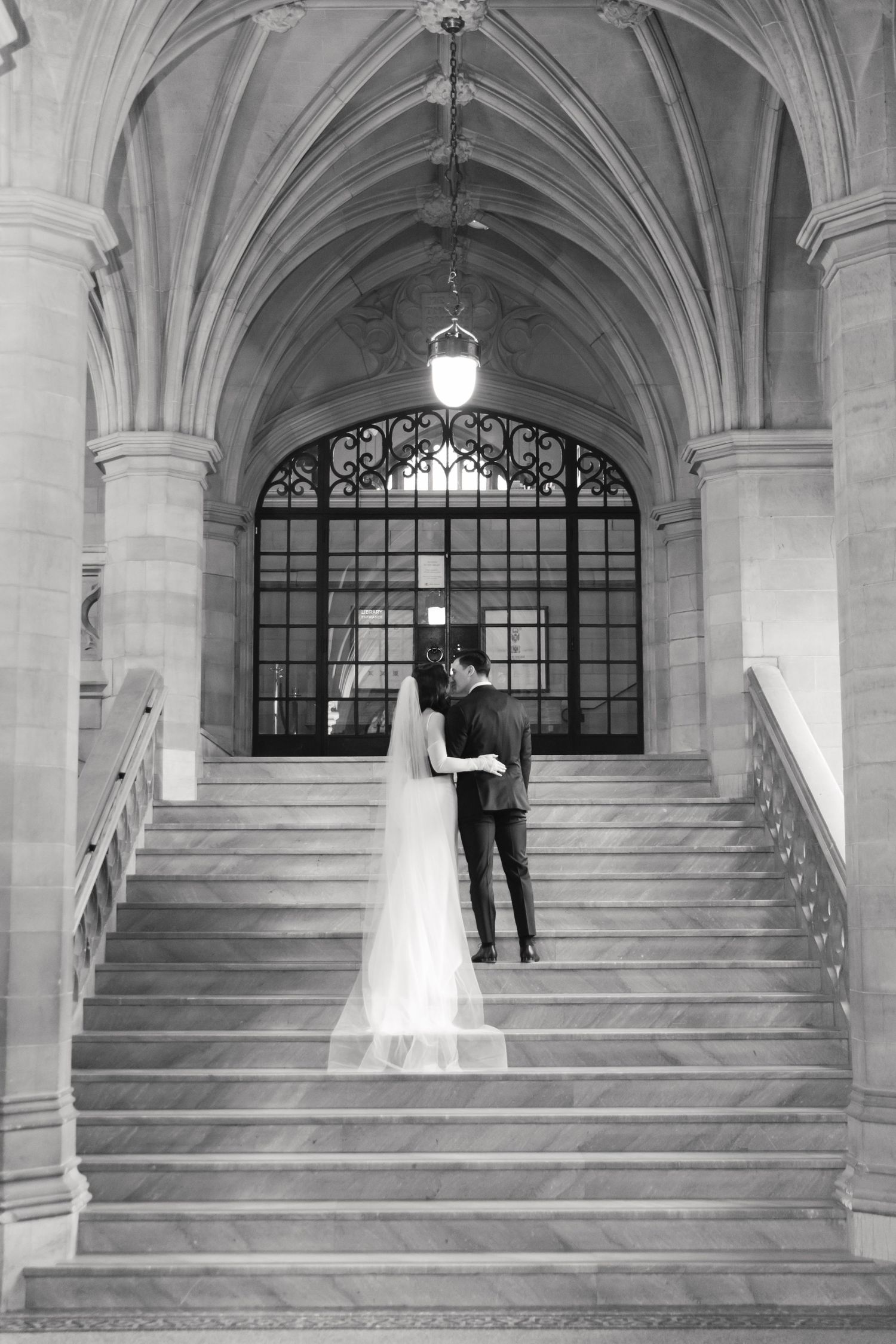 Black and white wedding photo on historic marble staircase with gothic architectural elements.