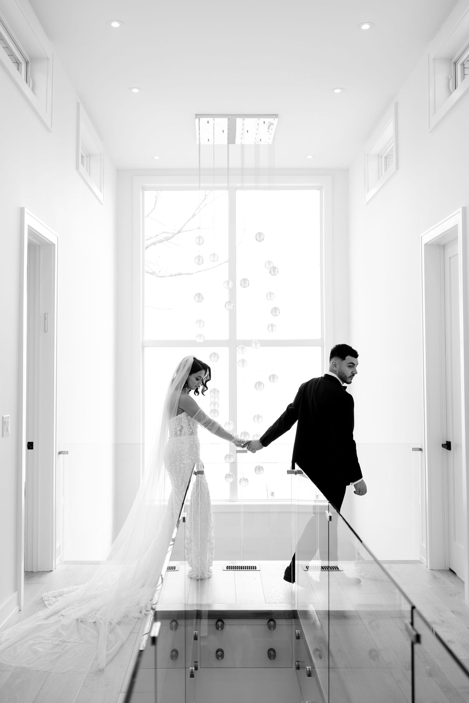 Black and white photo of couple holding hands while walking down modern bright hallway.