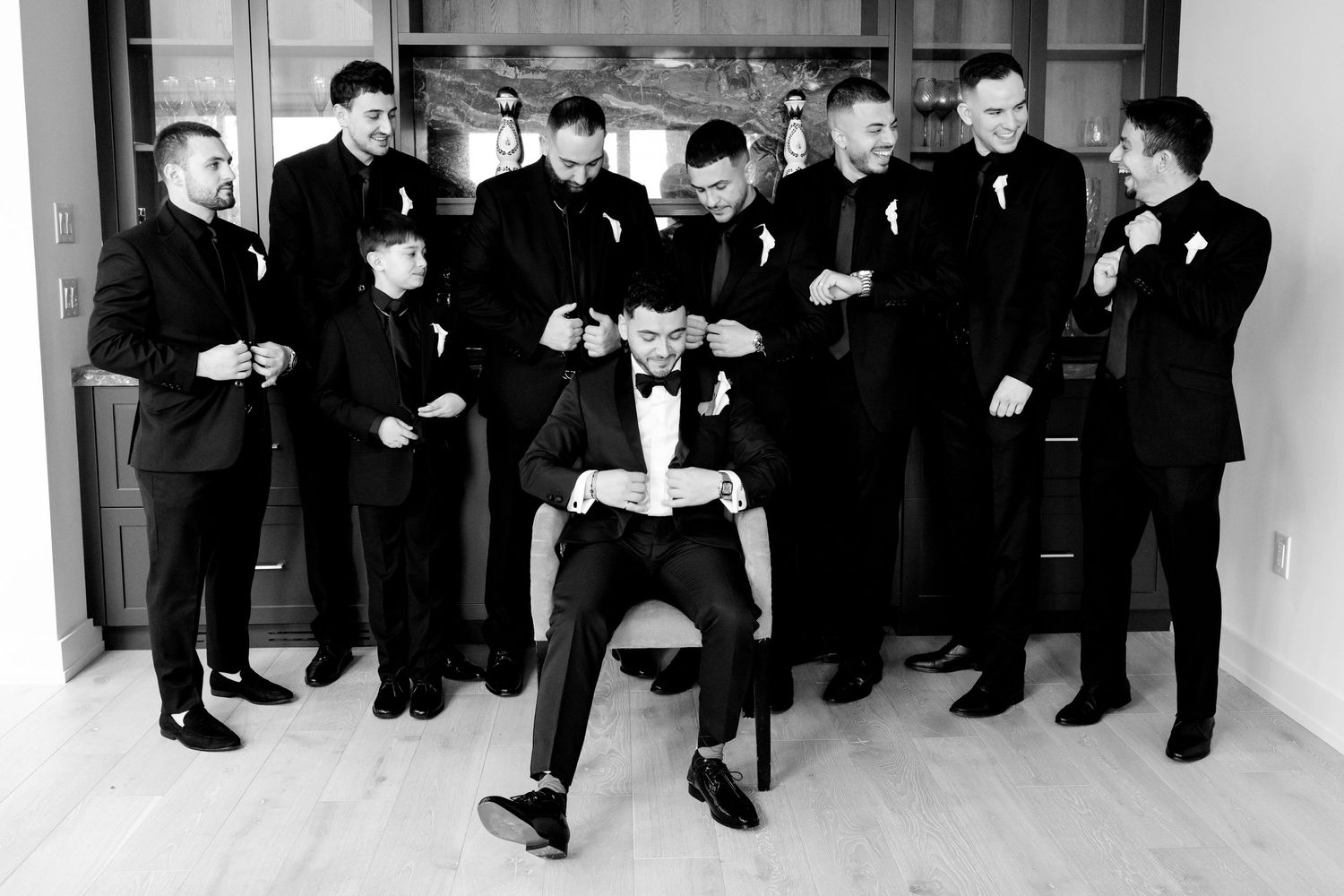 A black and white photo of groomsmen in suits posing for a stylized group photo indoors.