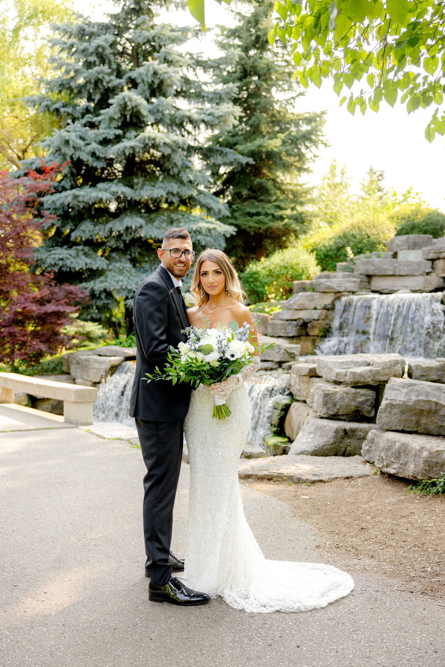 A wedding portrait showcasing a beautiful garden backdrop with stone waterfall and evergreen trees.