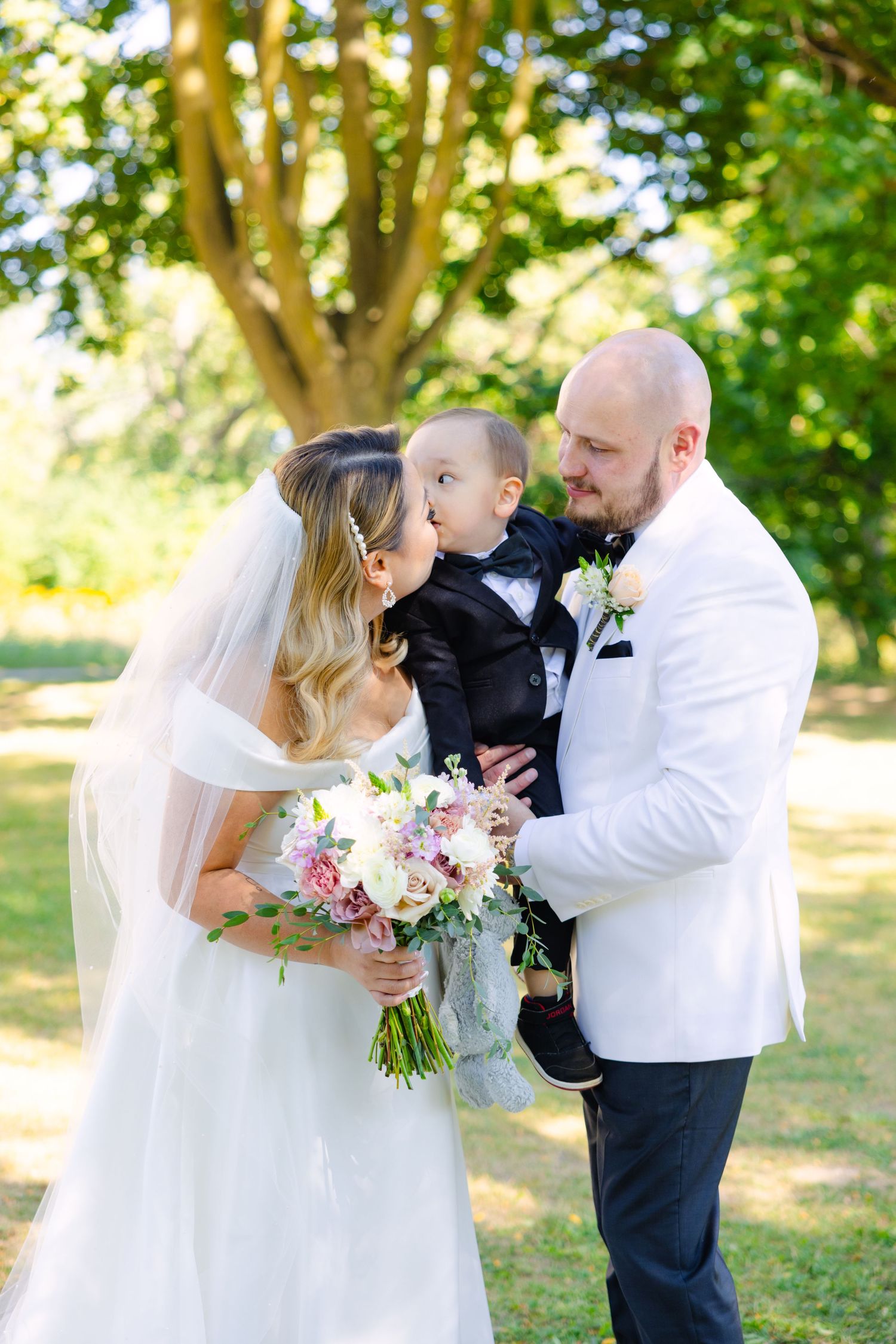 Sweet family moment captured during outdoor wedding with bride holding pink floral bouquet.