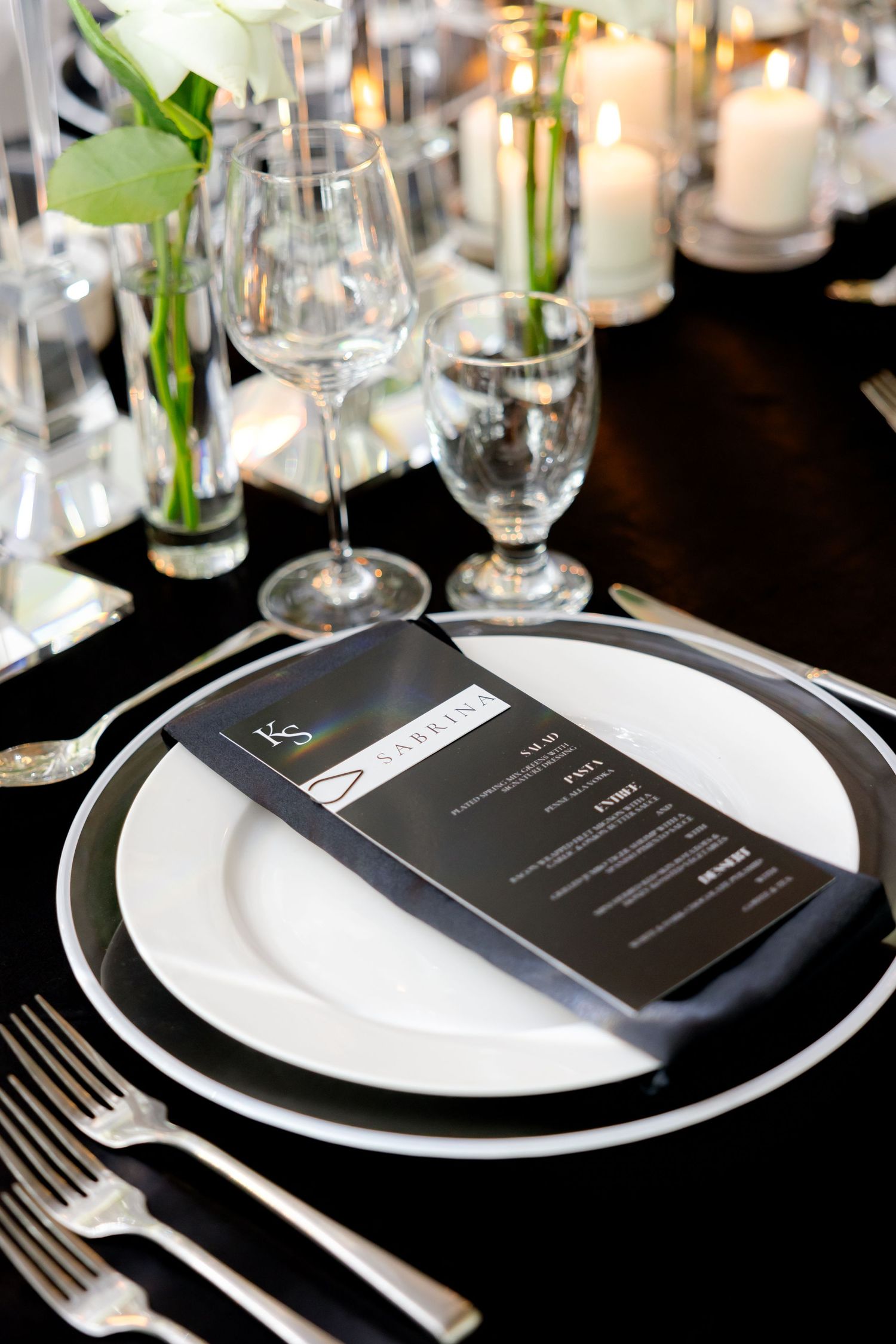 Black and white place setting with menu card, wine glass, and white floral accents.