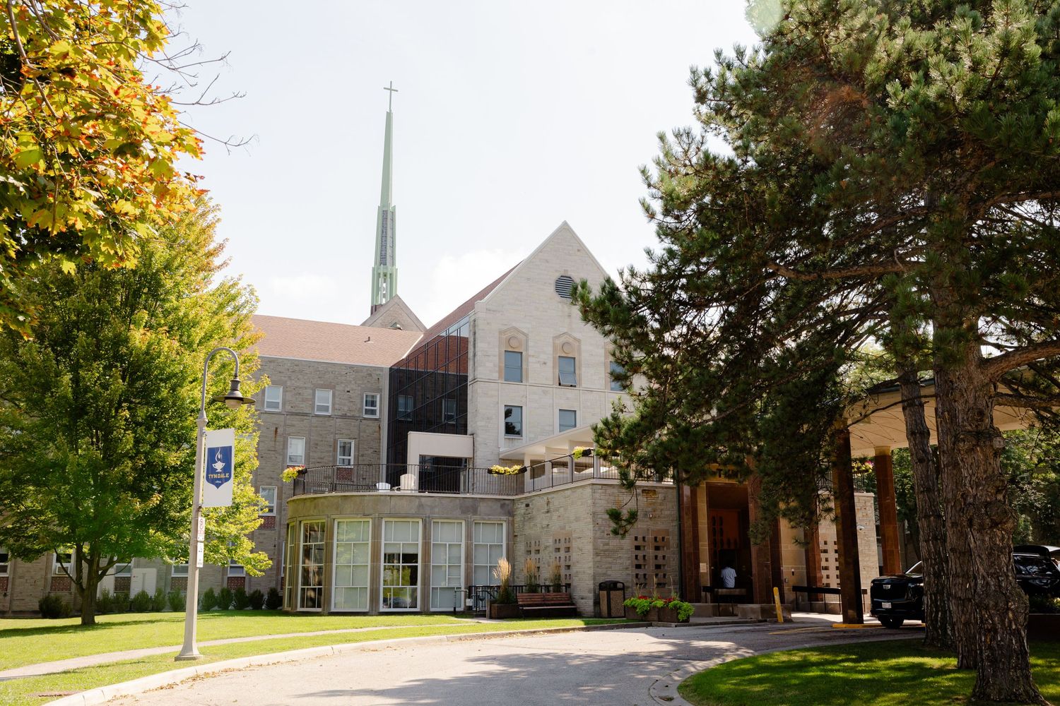 Modern church building with tall spire and white facade surrounded by autumn trees on a sunny day.