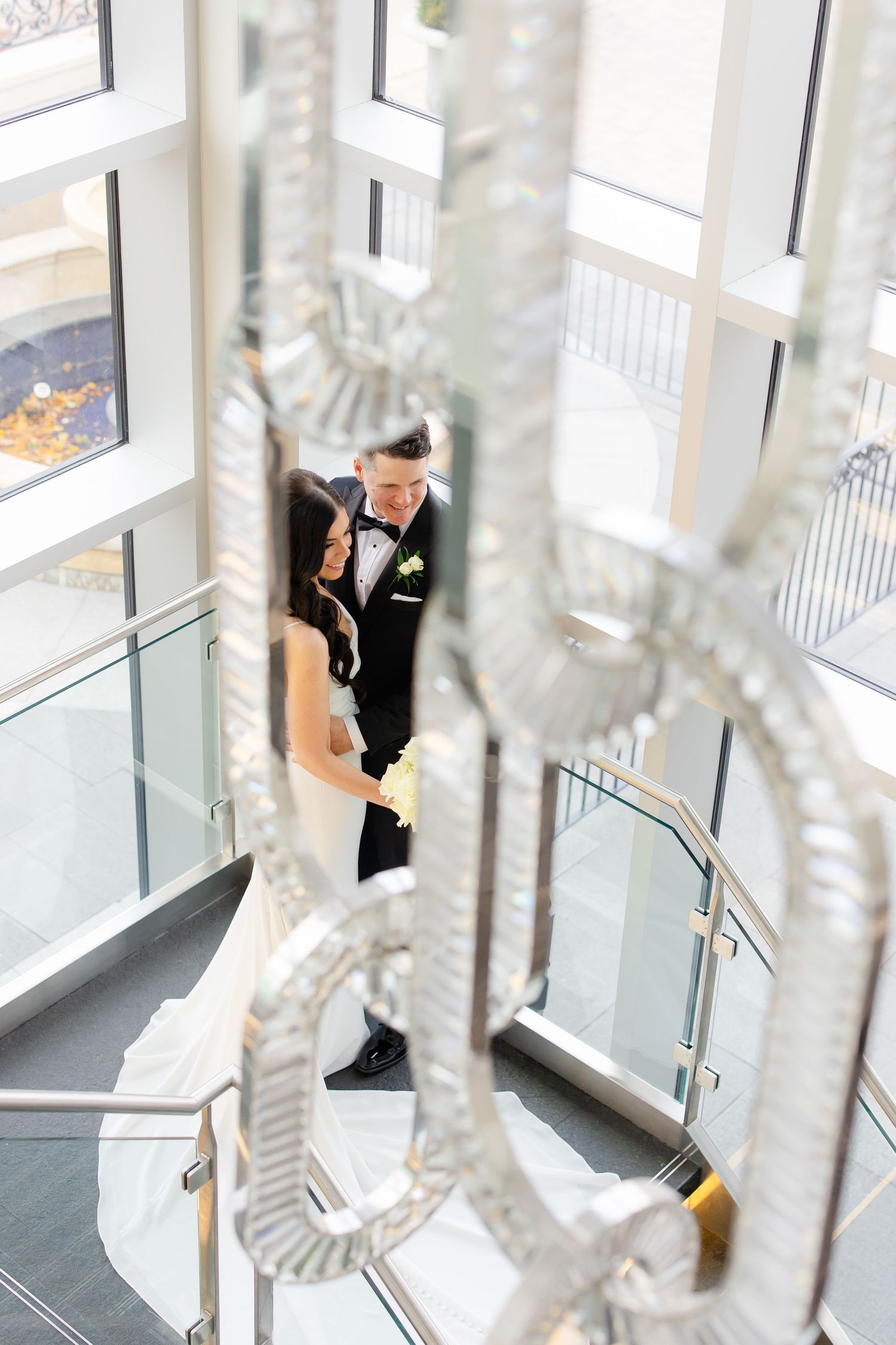 Artistic wedding photo through crystal chandelier in modern glass building.