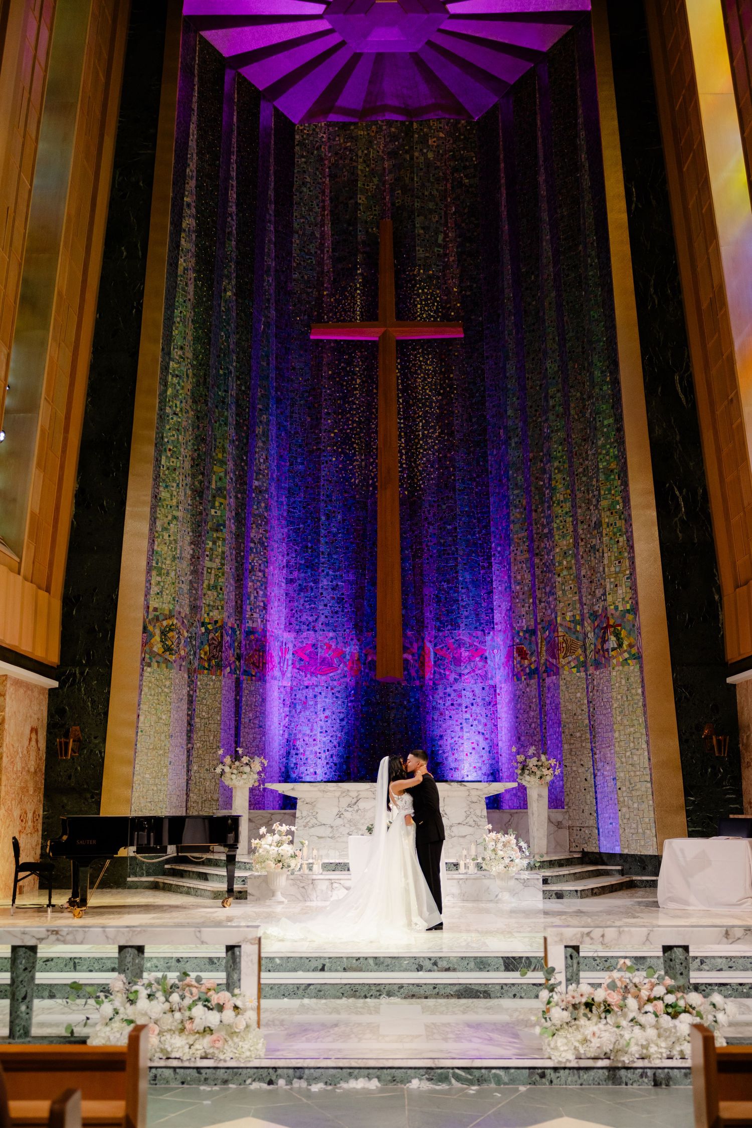 A couple shares their first dance in a church with dramatic purple lighting and a large cross backdrop.