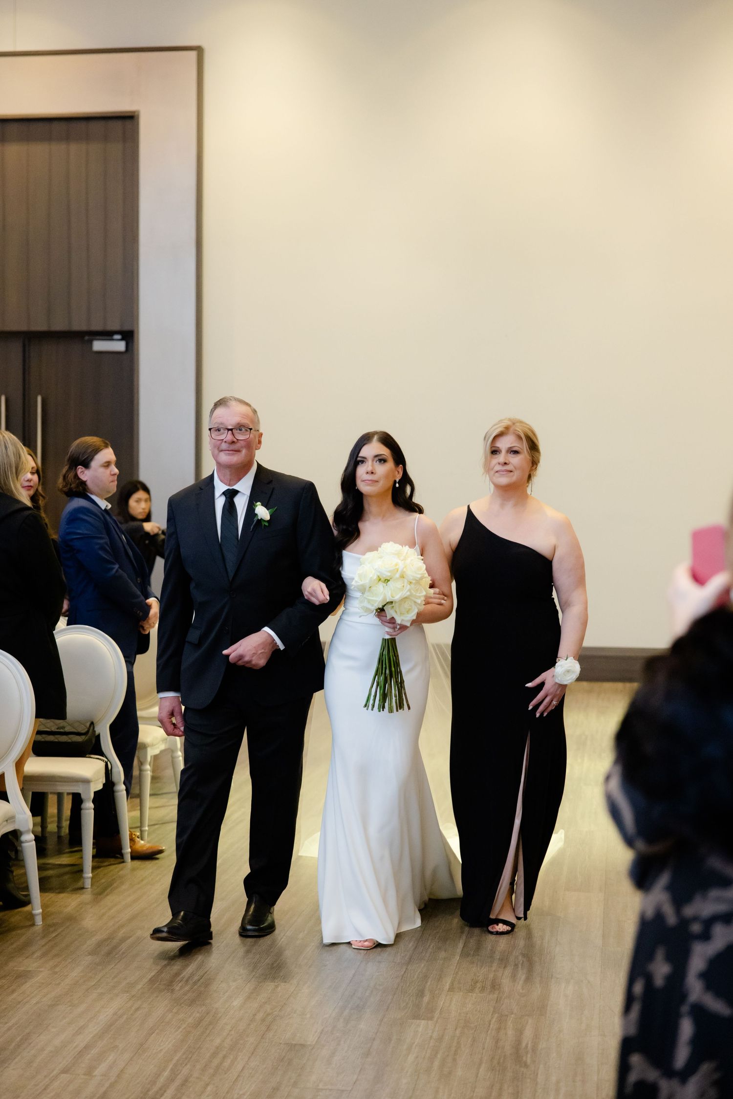 Wedding party members escort bride in elegant white gown down the ceremony aisle.