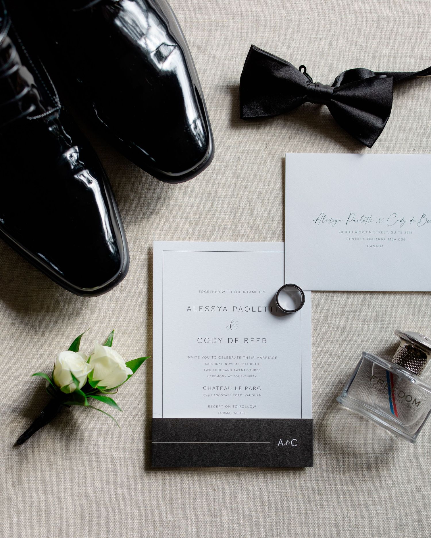 Wedding details flatlay with black dress shoes, bow tie, invitation and rings on beige linen.