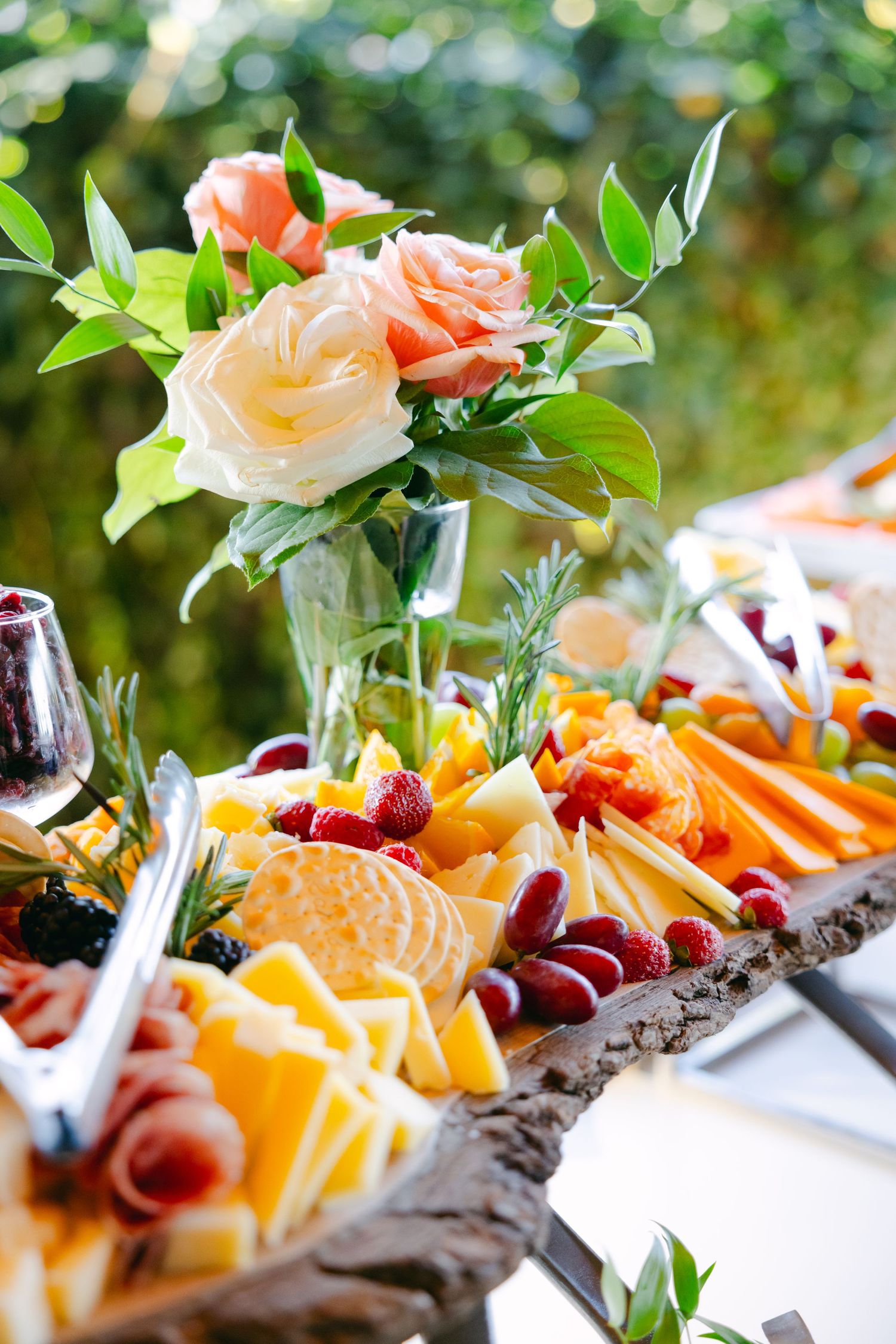 Beautifully arranged fruit and cheese platter with floral centerpiece at an outdoor event.