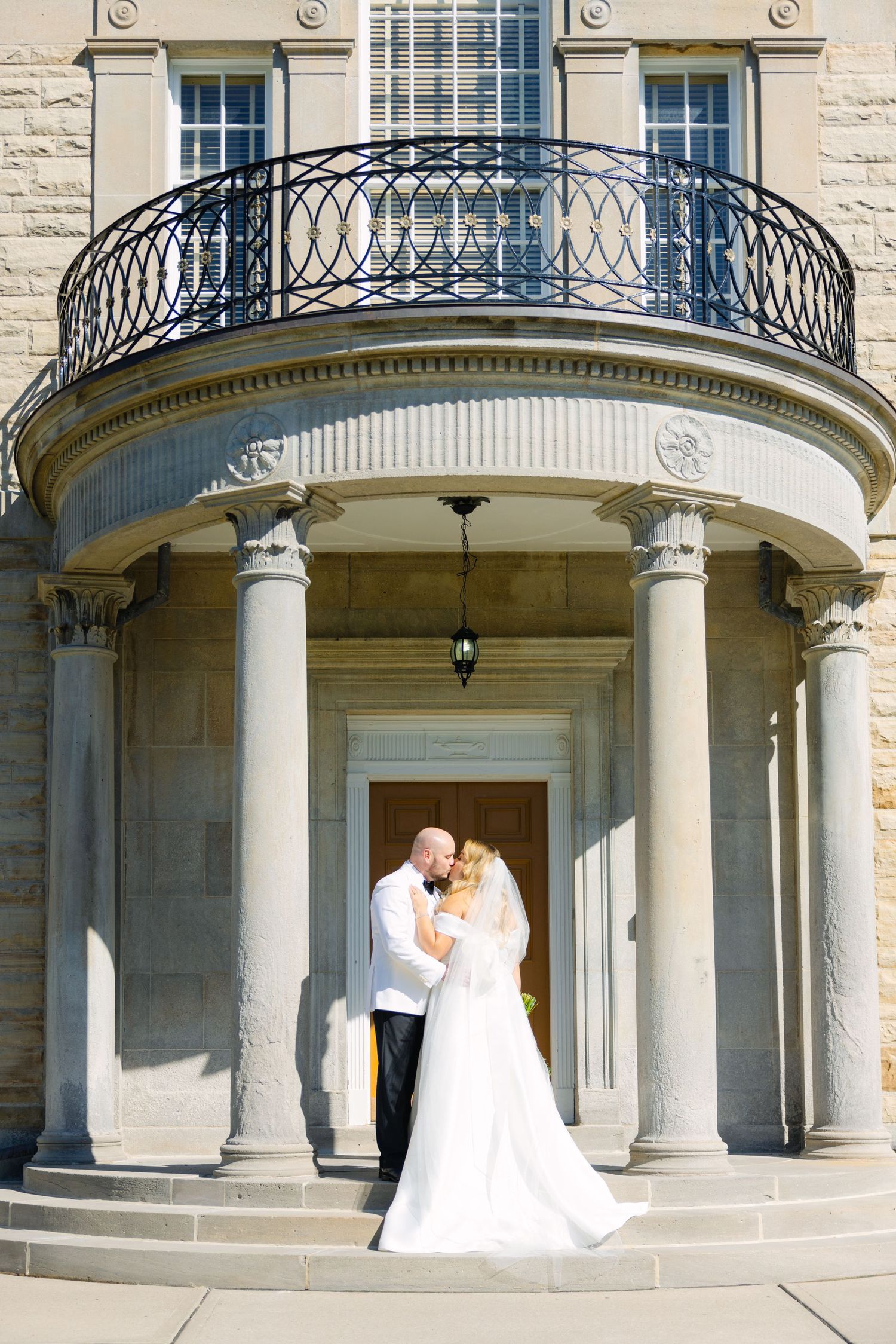 Wedding moment captured under a grand portico with decorative ironwork and limestone columns.