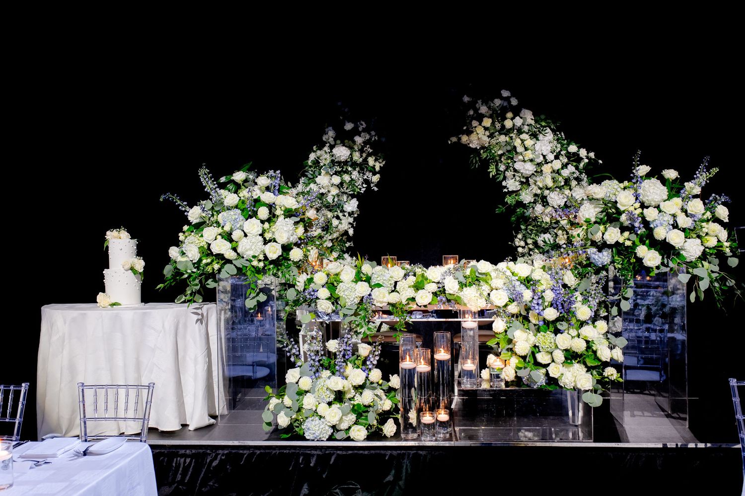 Wedding ceremony backdrop featuring abundant white floral arrangements and romantic lighting.