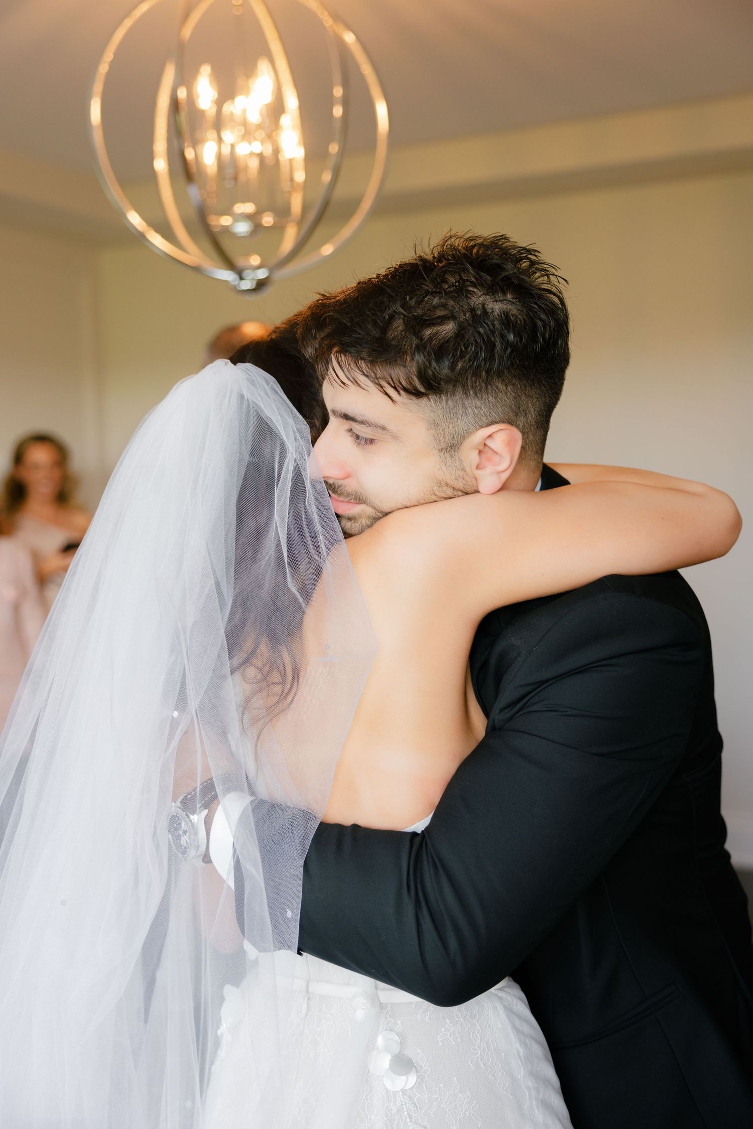 A tender embrace between the newlyweds under an elegant spherical chandelier during their wedding celebration.