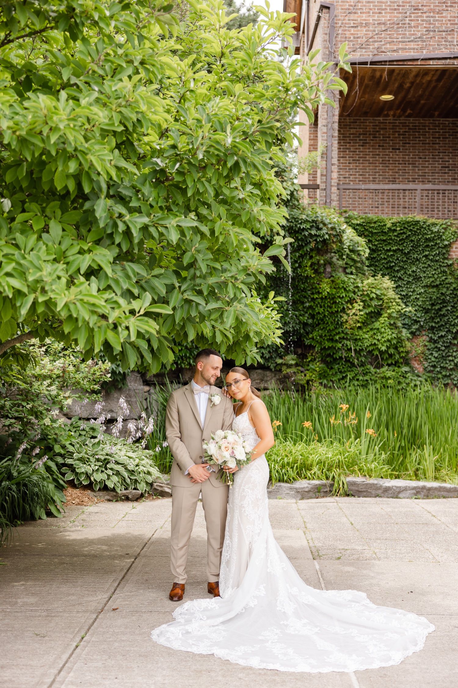 Garden wedding portrait with dramatic lace train against ivy-covered brick wall.