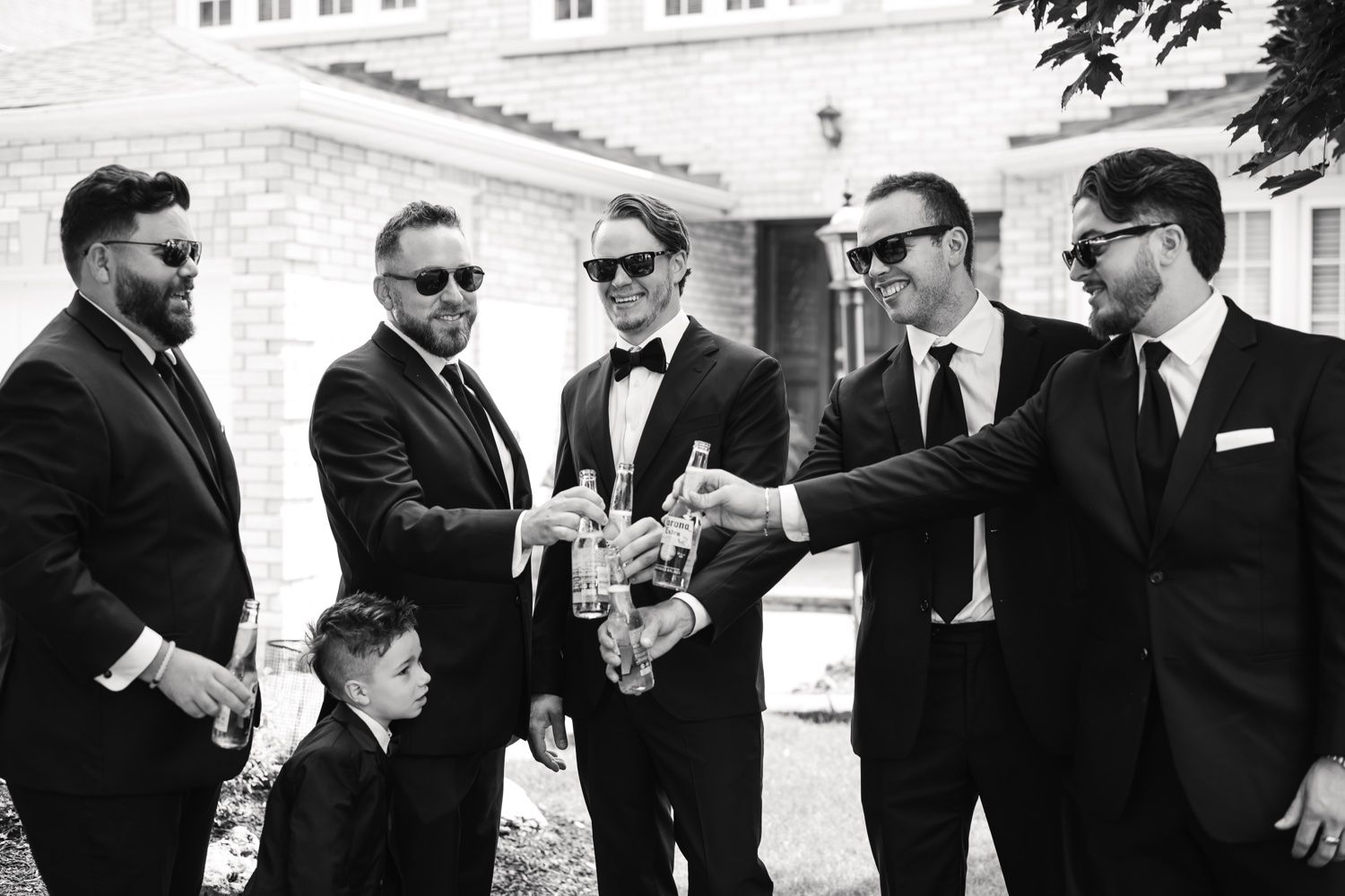 Black and white photo of groomsmen toasting with drinks outdoors.