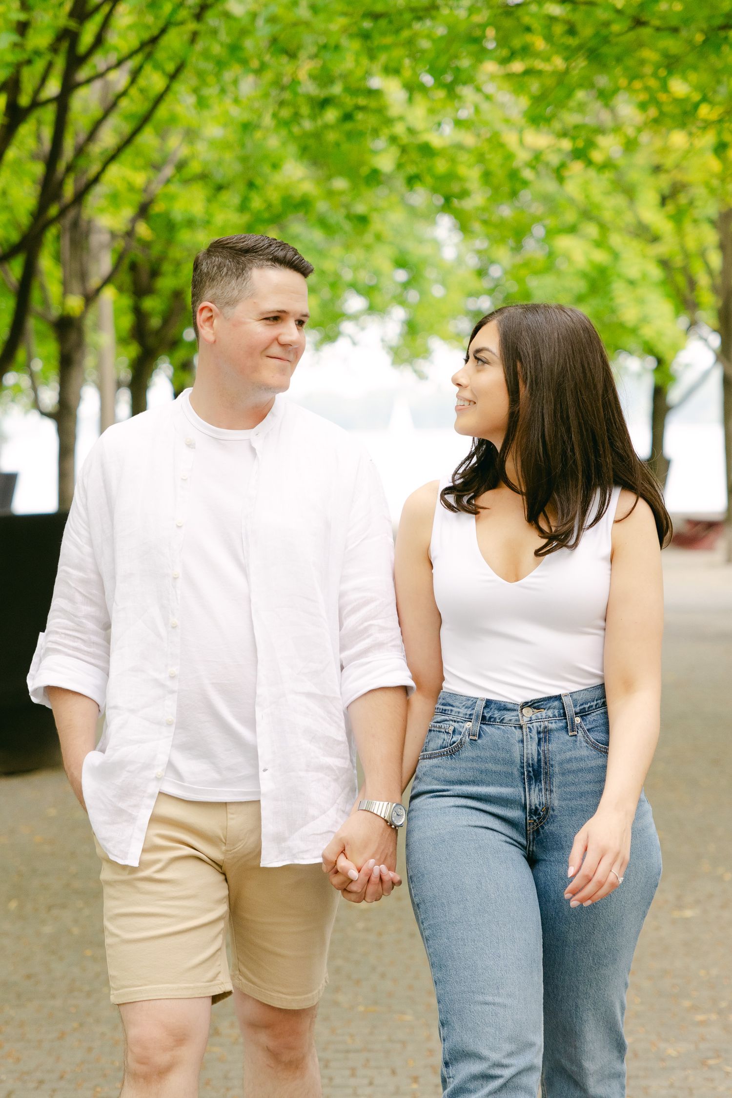 A couple shares a tender moment while walking beneath green trees.