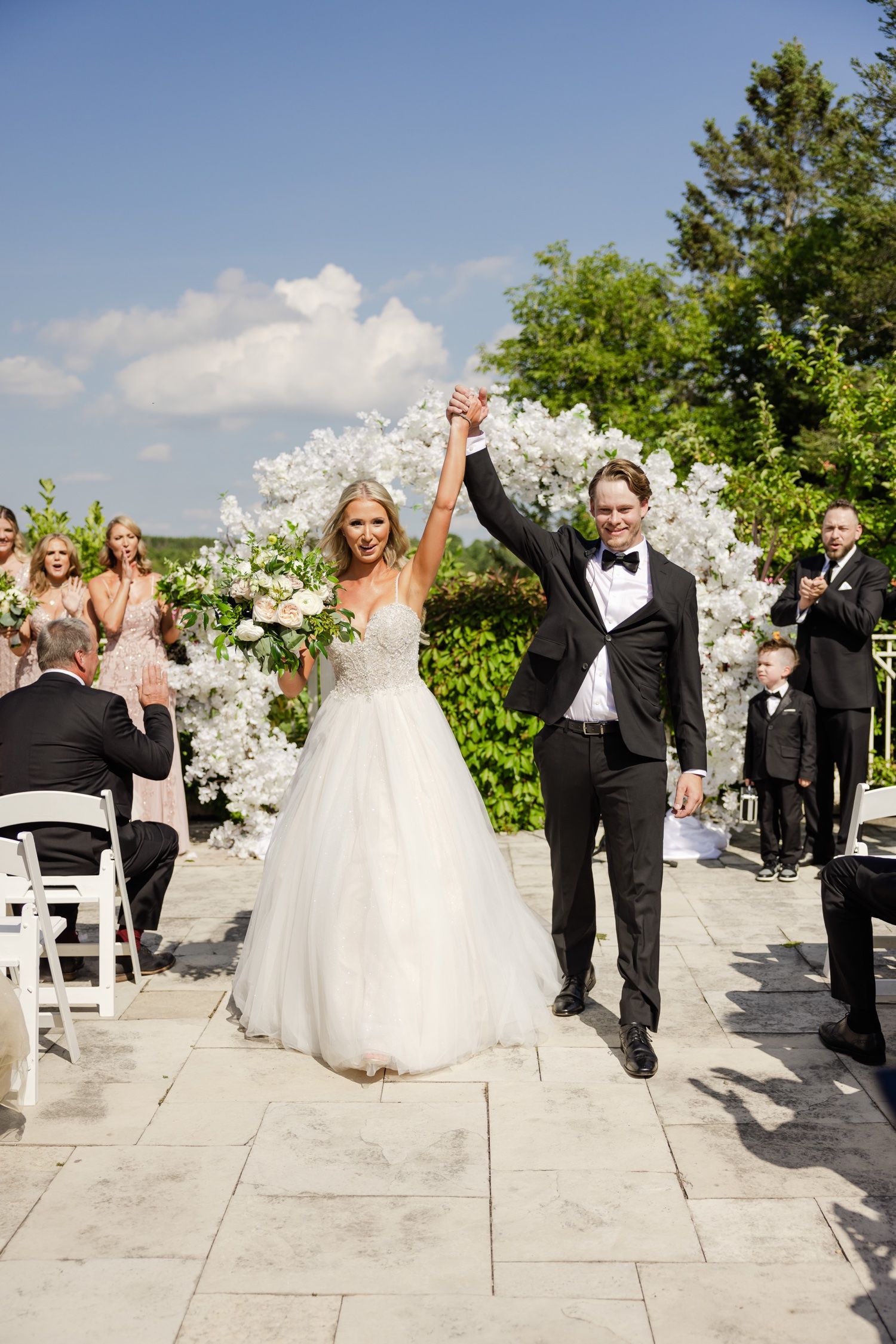 Triumphant newlyweds celebrate with raised hands while guests applaud on their wedding day.