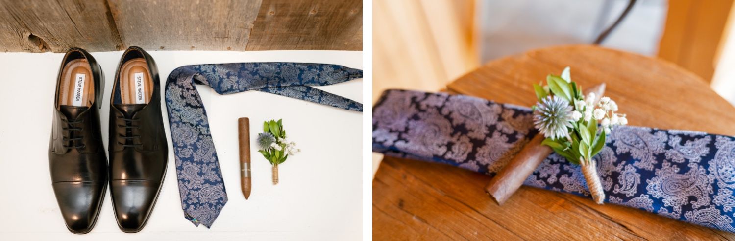 Wedding accessories including black dress shoes, blue patterned tie, and boutonniere laid out on wooden surface.