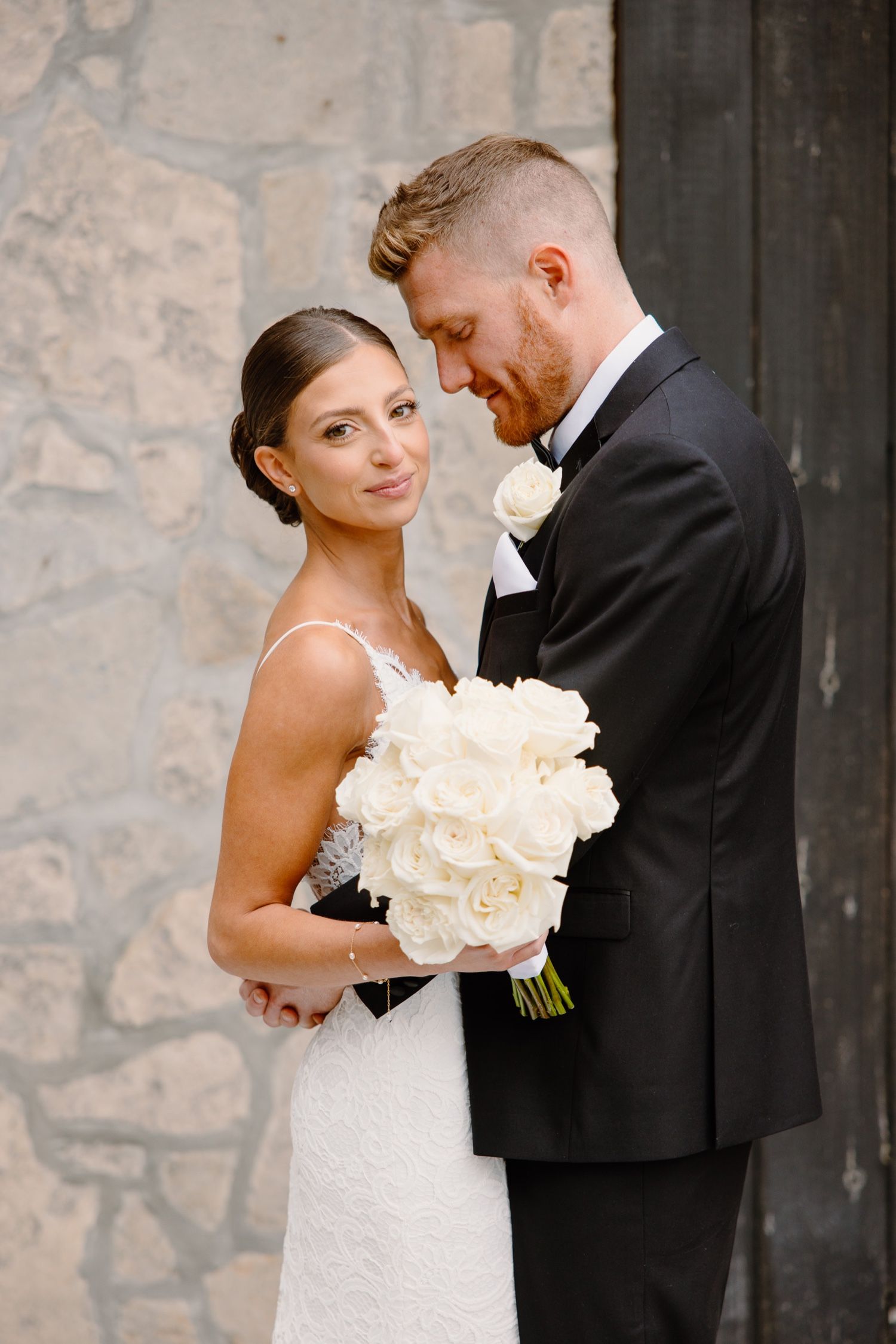 Intimate wedding portrait with white roses against stone and wooden backdrop.