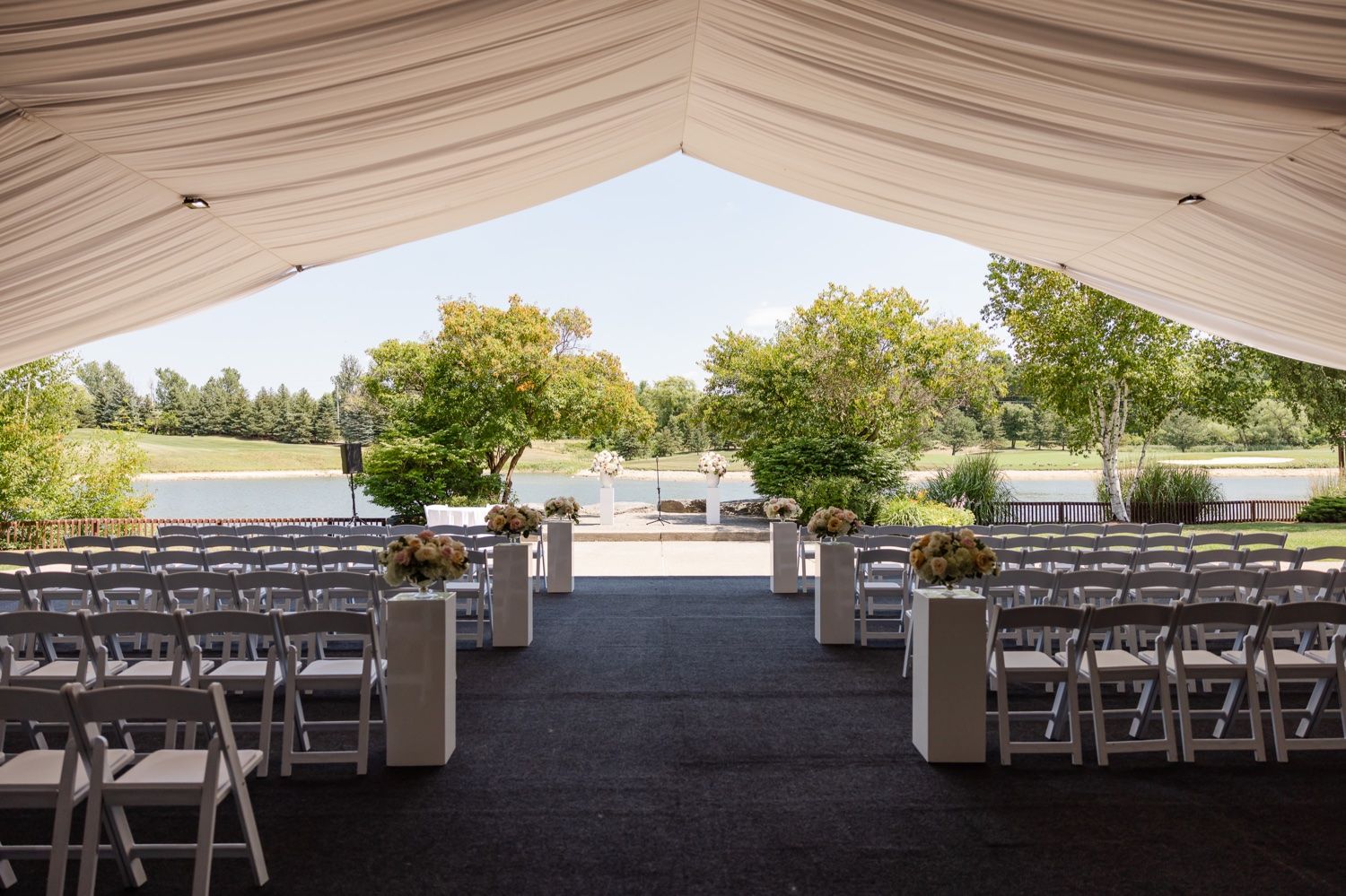 An elegant outdoor wedding ceremony setup with white chairs under a draped tent canopy.