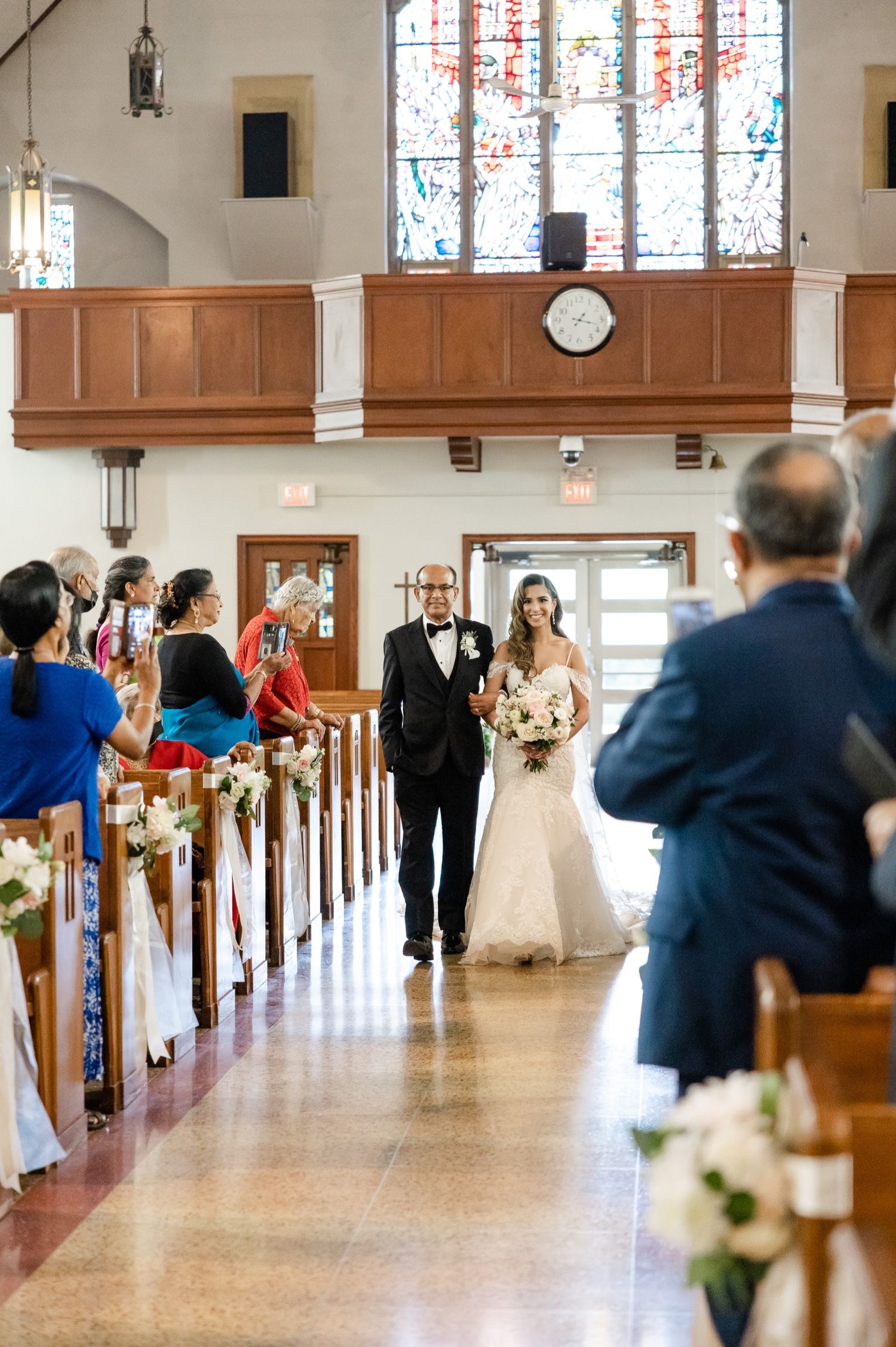 A wedding ceremony processional in a church with wood paneling and stained glass windows.