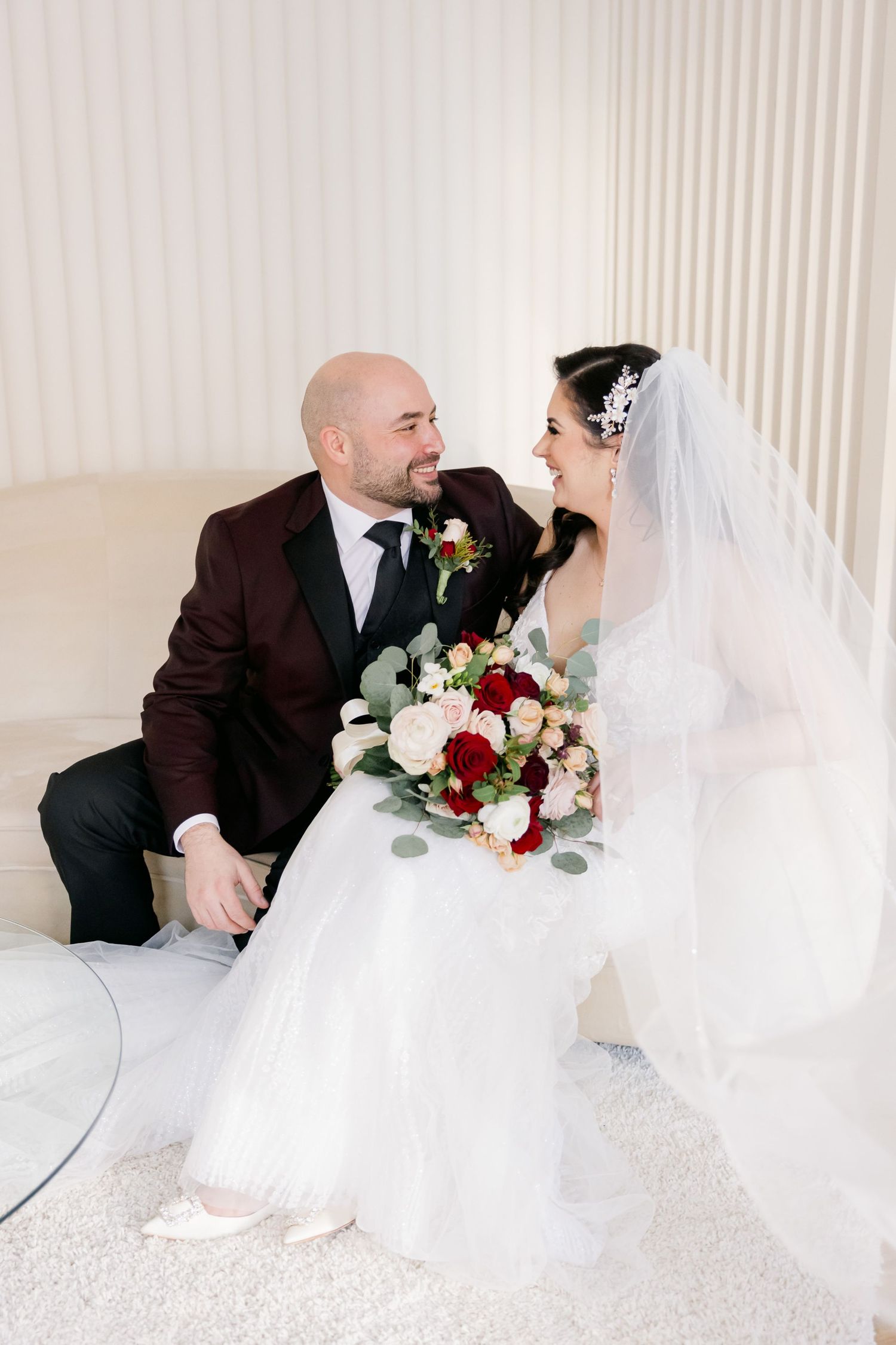 Wedding couple sitting on white chair with elegant burgundy and blush bouquet.