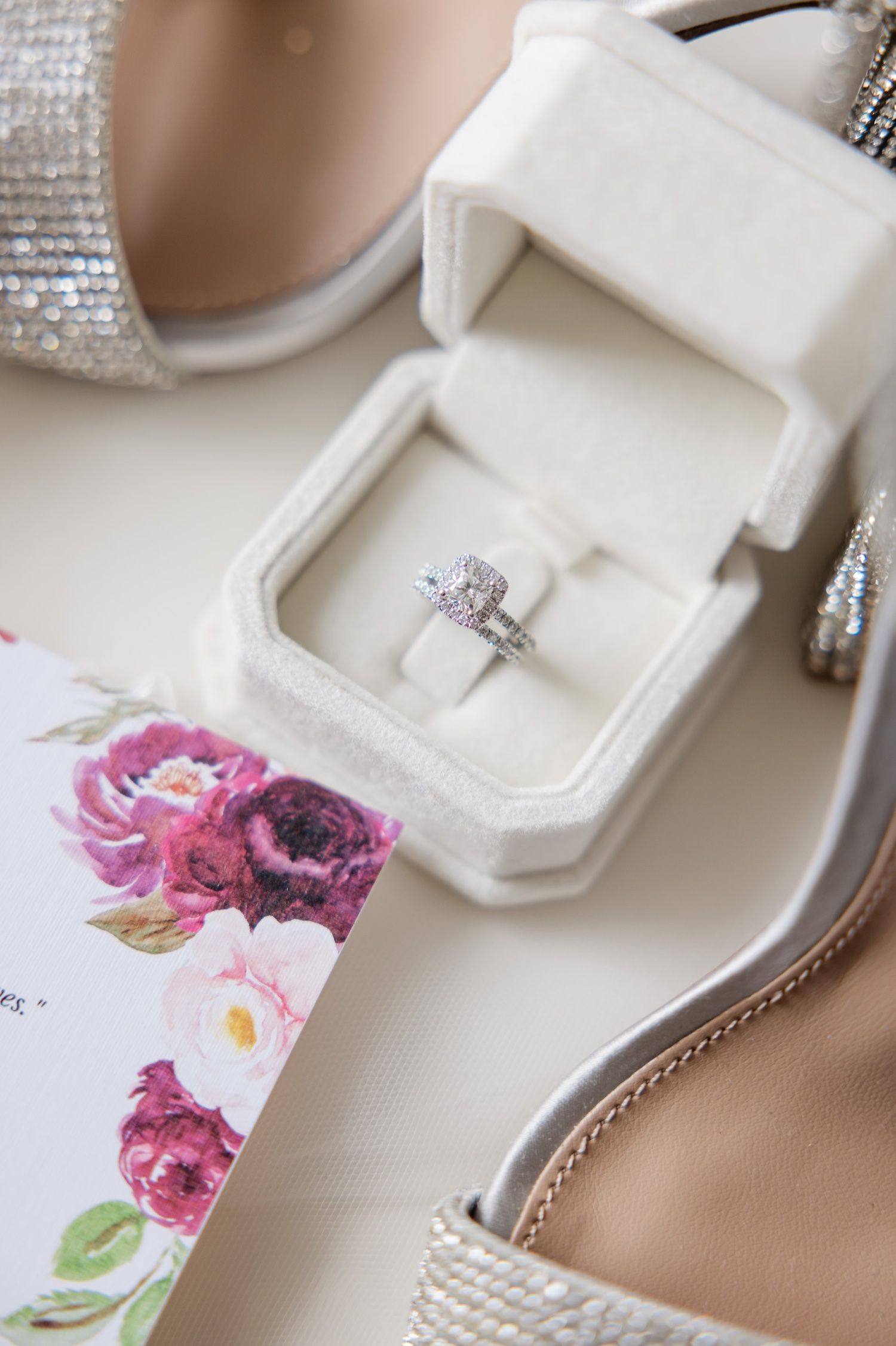 Wedding ring in white box with floral invitation featuring pink and burgundy flowers.