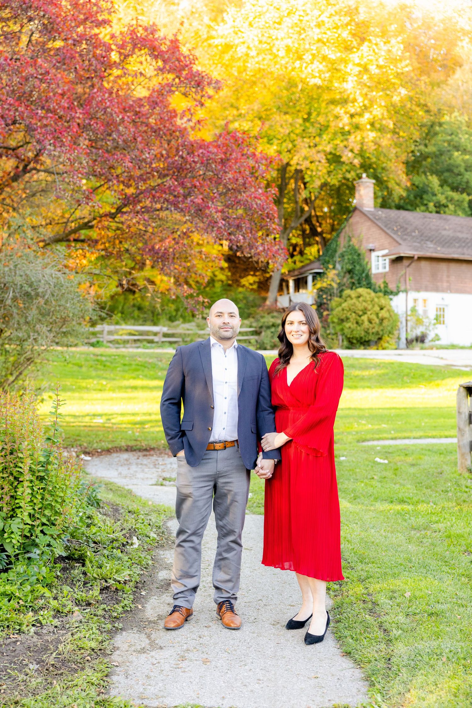A couple poses on a garden path with stunning fall colors and a cottage in the background.