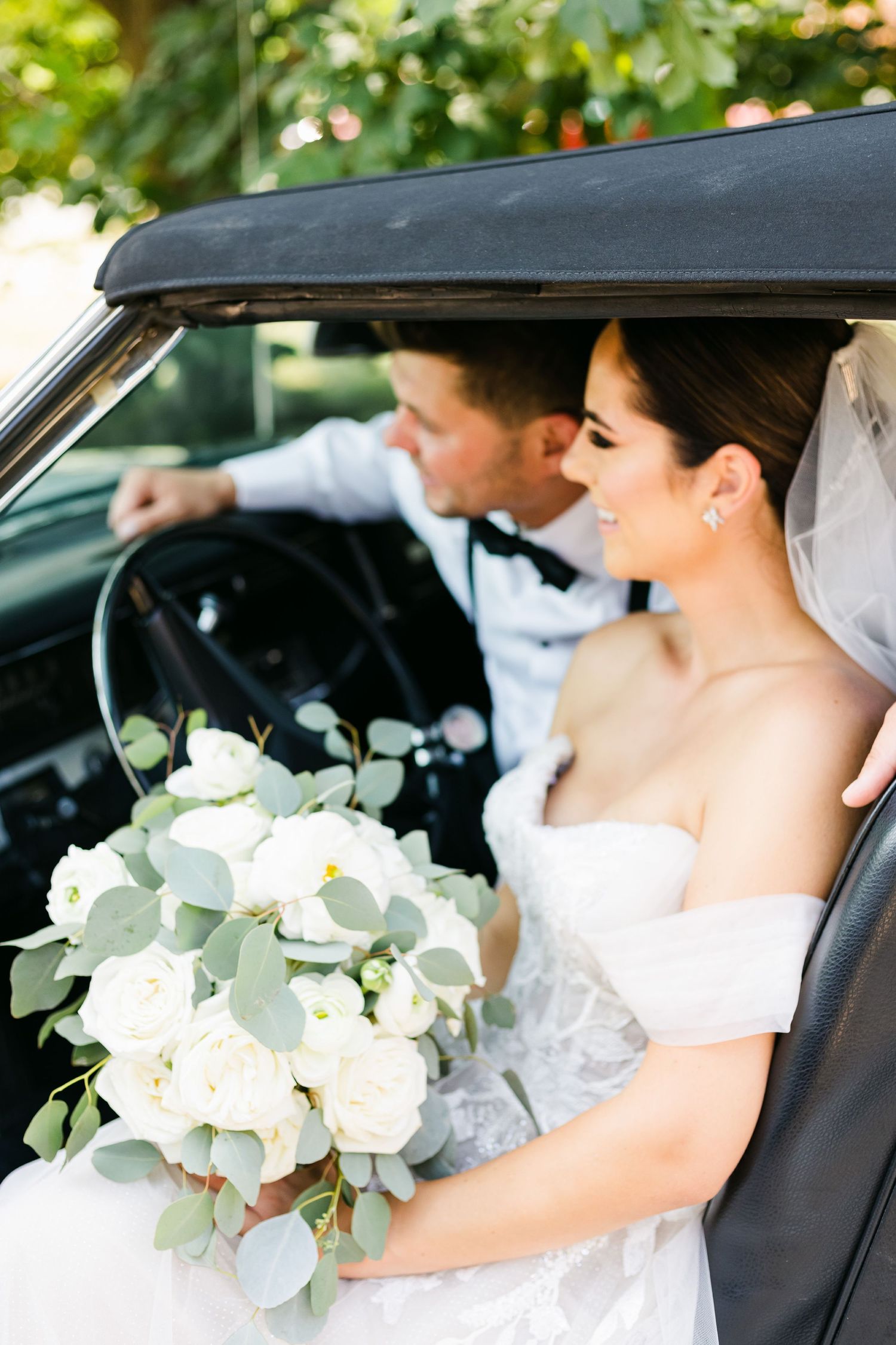 Elegant wedding photo inside vintage car with white and eucalyptus bouquet.
