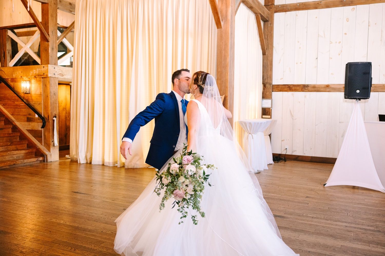 Romantic dance moment in a rustic barn venue with wooden beams and soft drapery.