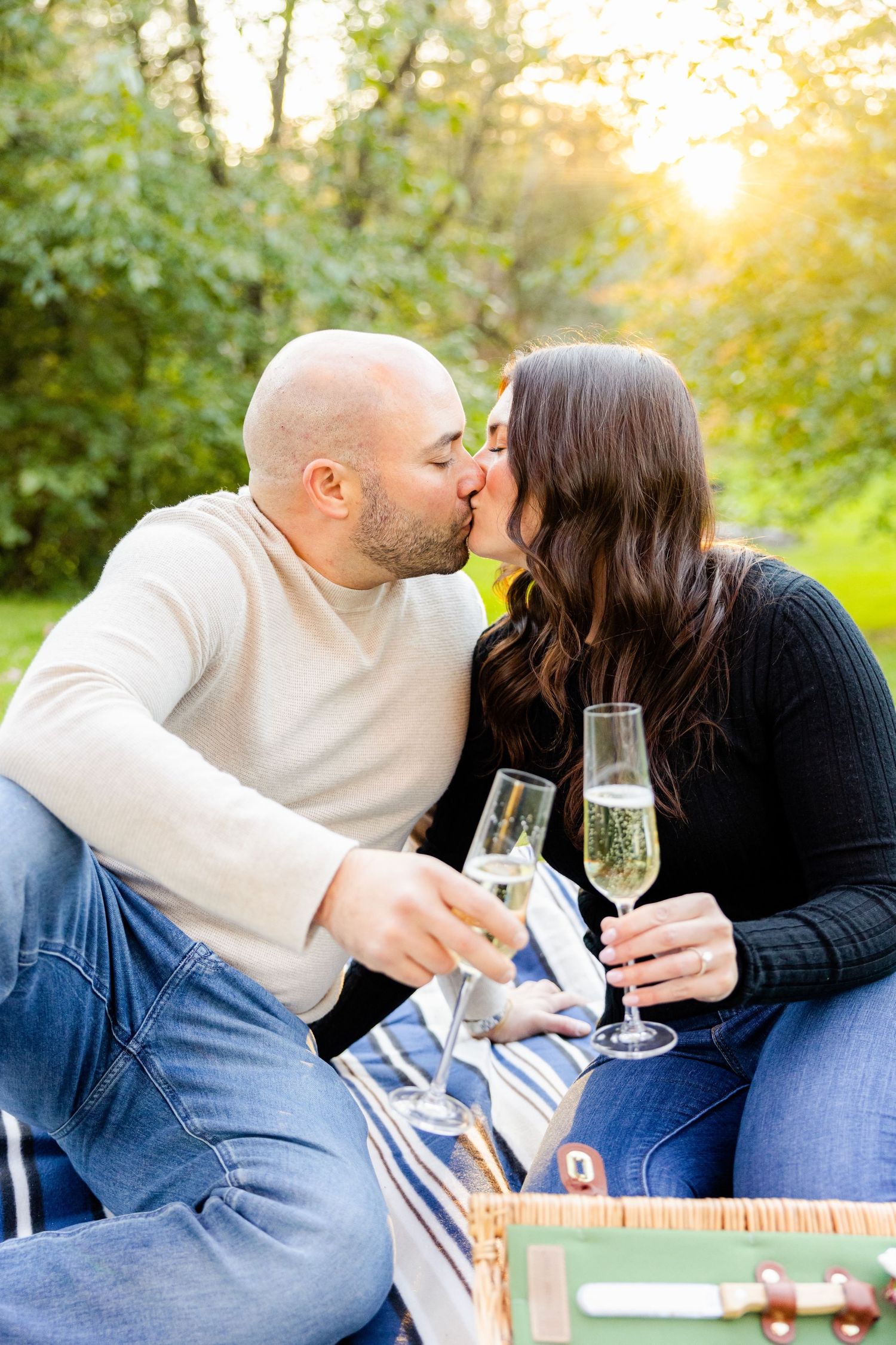 Romantic sunset kiss shared during champagne picnic in garden setting.