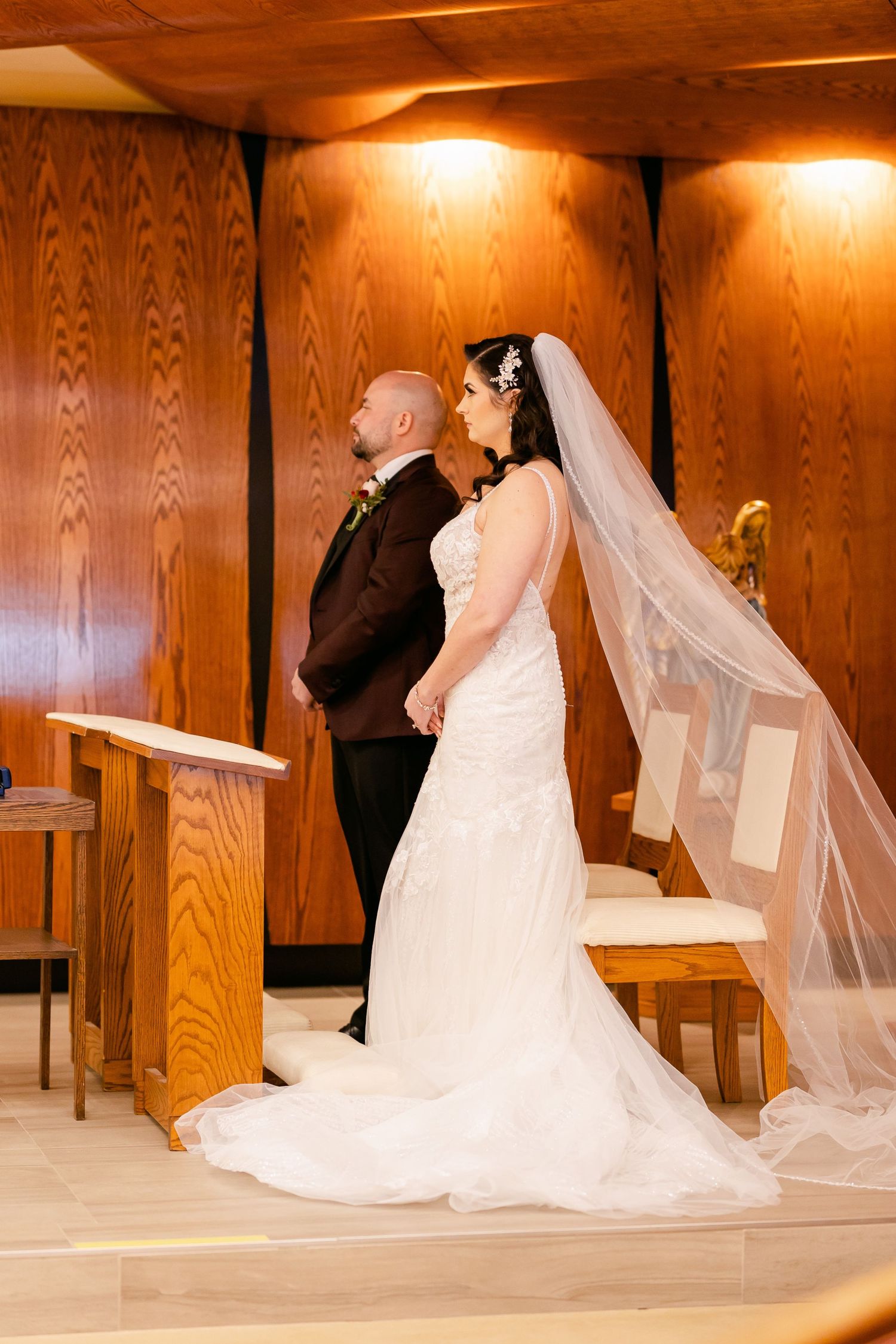 A wedding couple stands at the altar in a wood-paneled church with warm lighting.