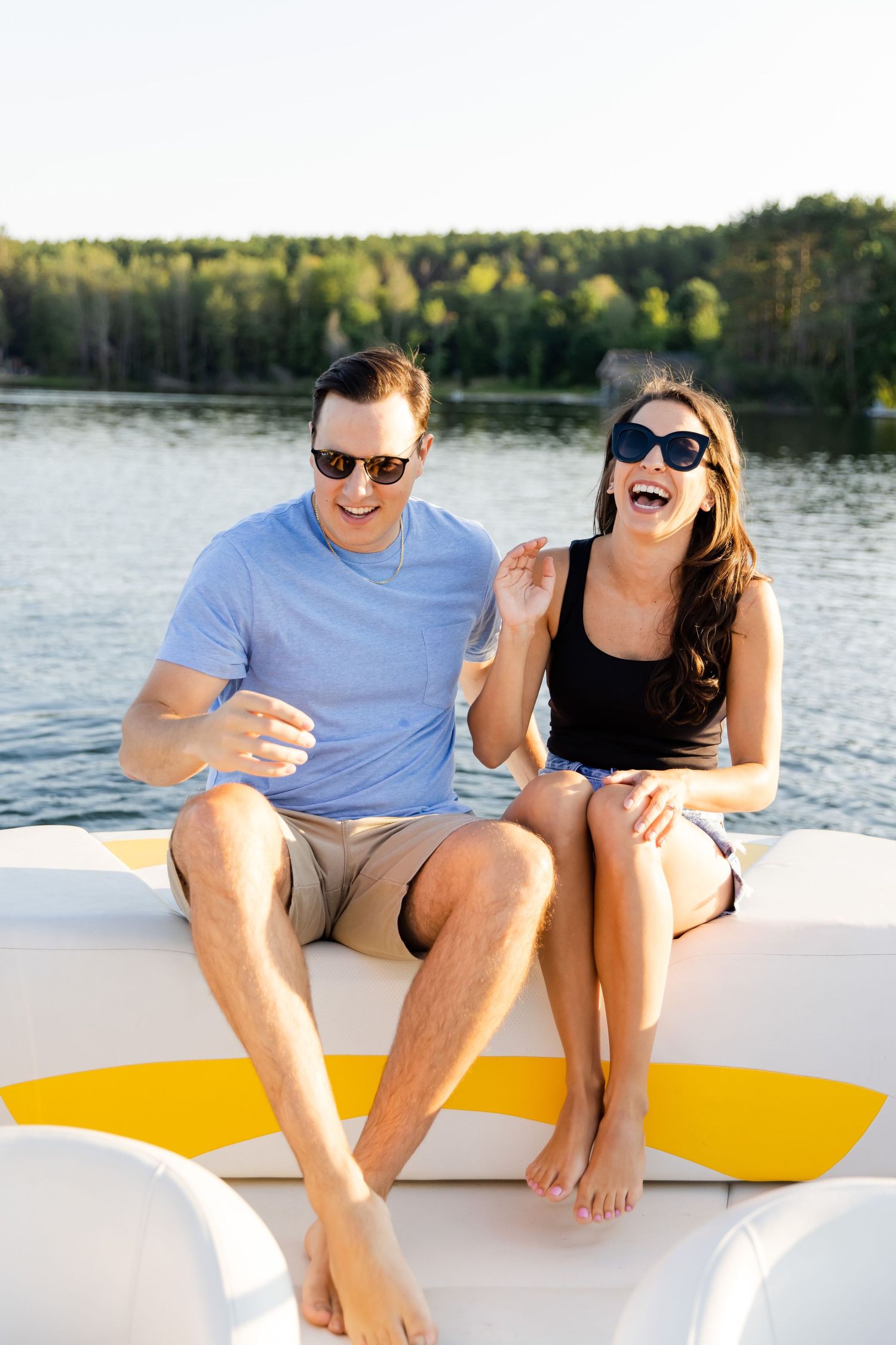 Couple laughing together while relaxing on boat deck during summer lake day.