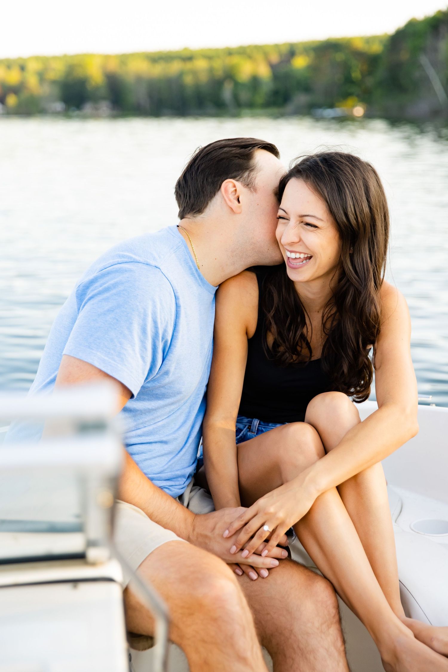 A sweet moment between a couple on a boat with sunlit trees in the background.