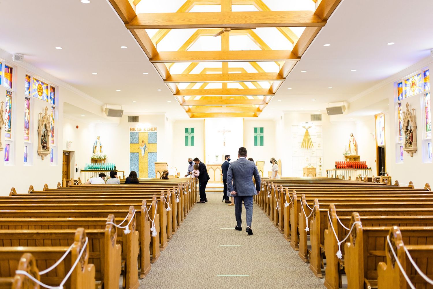 A church interior with wooden pews and stained glass windows illuminated by natural light.