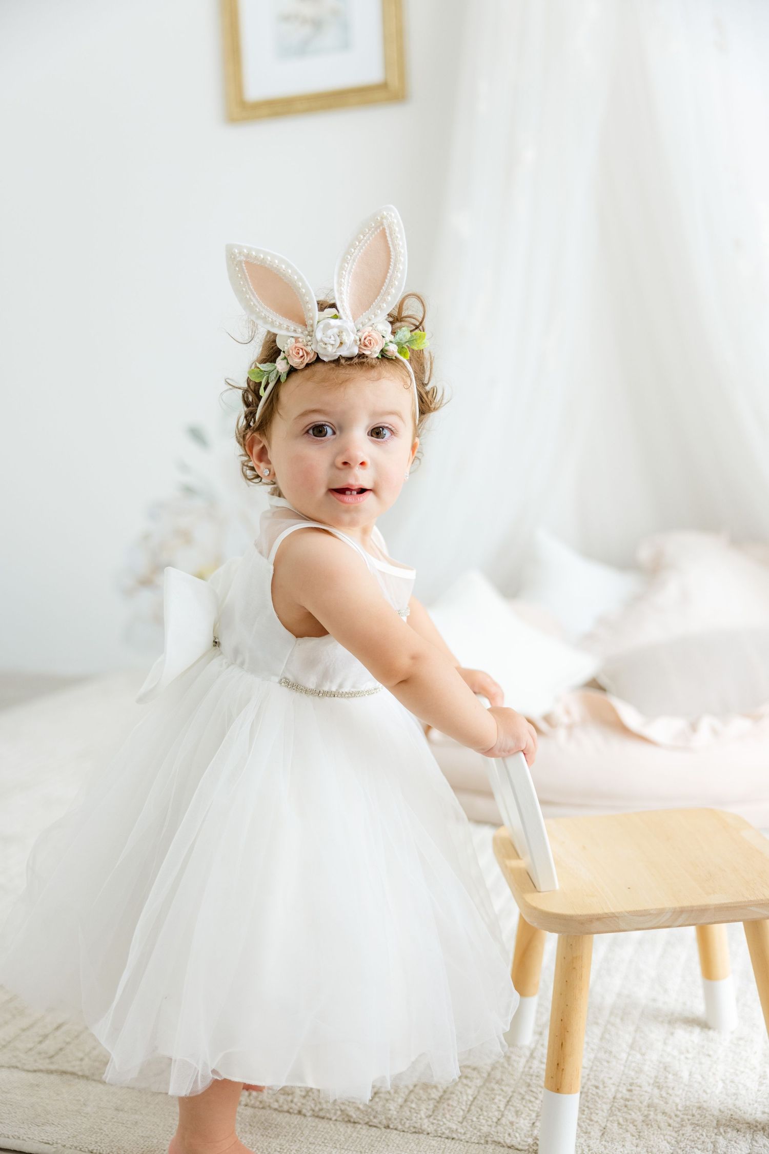 A whimsical spring photoshoot features a white tulle dress and bunny ear headpiece with floral accents.