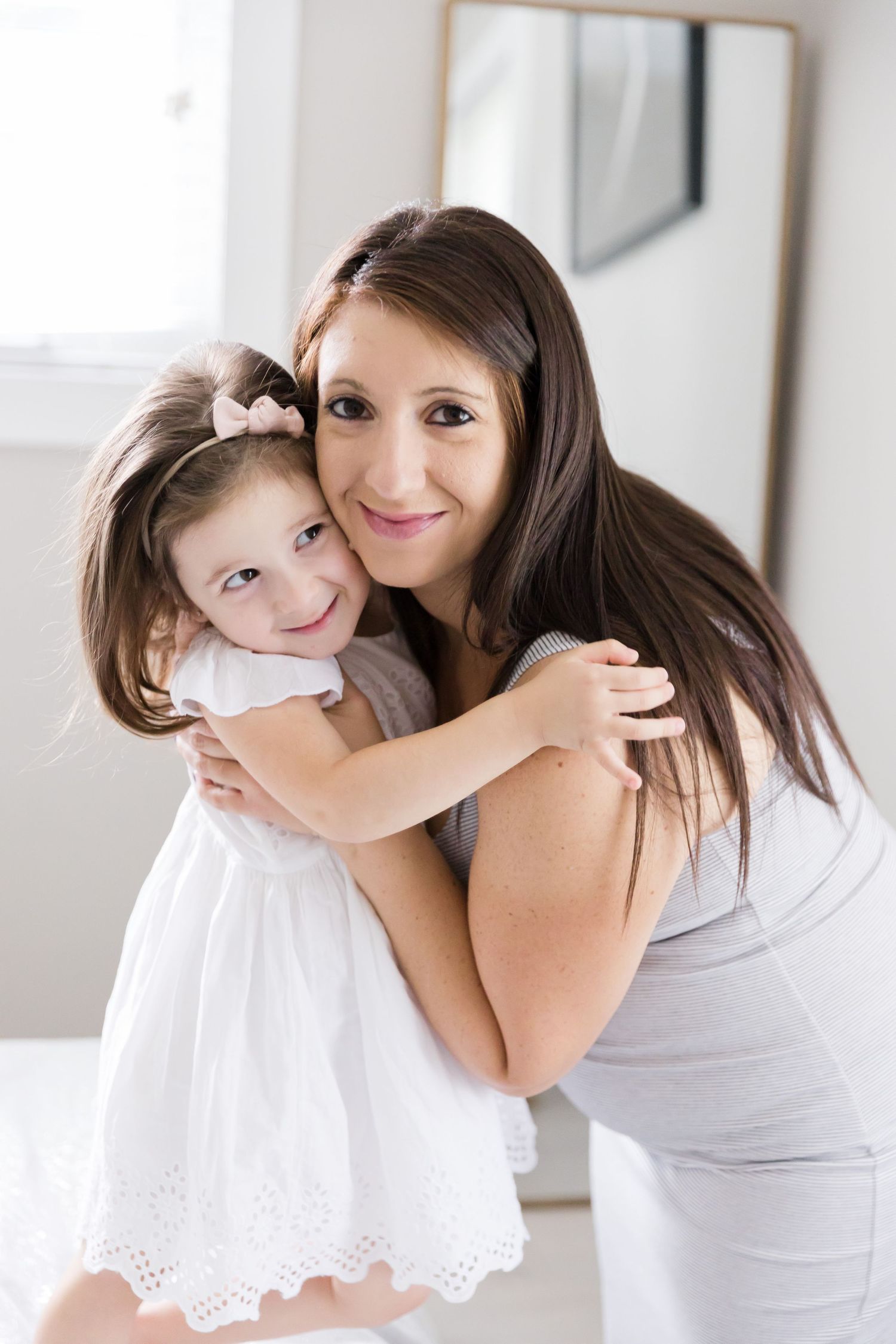 Mother and daughter embracing and smiling in bright white room.
