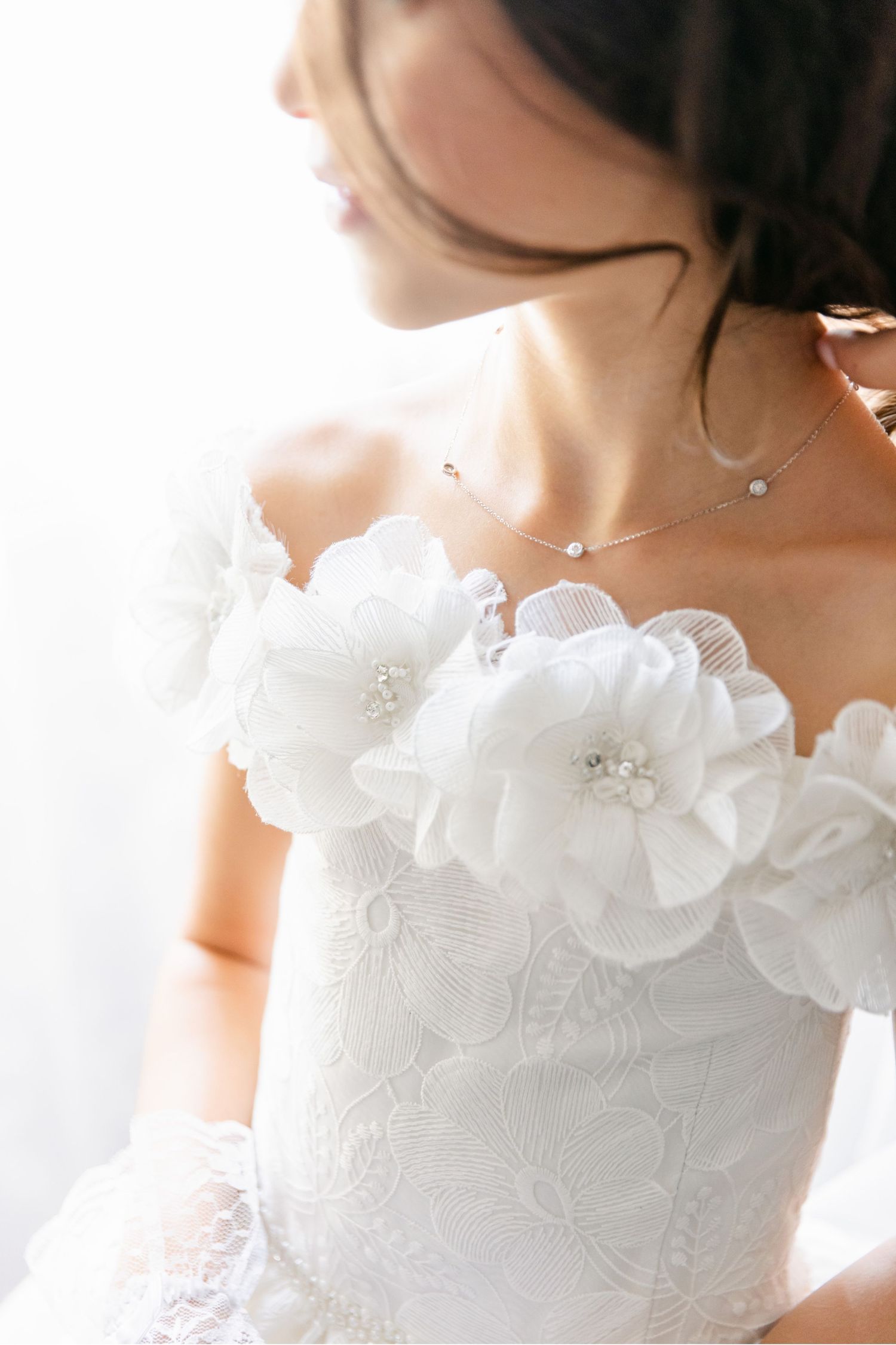 Close-up detail of white organza flowers adorning the neckline of a wedding gown with delicate beading.