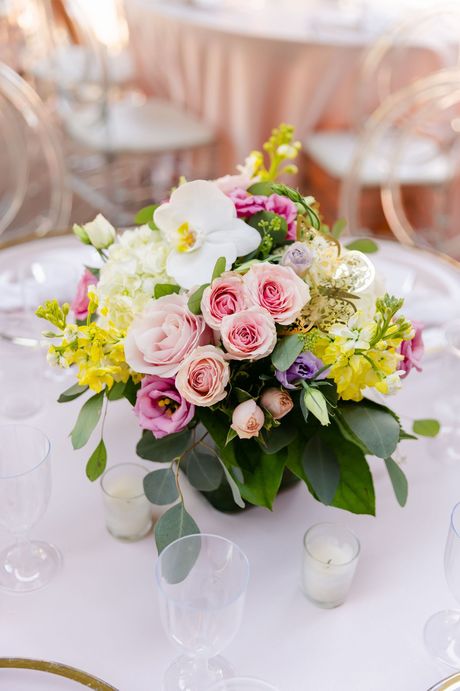 Beautiful floral centerpiece with pink roses, white flowers and greenery on an elegant table setting.
