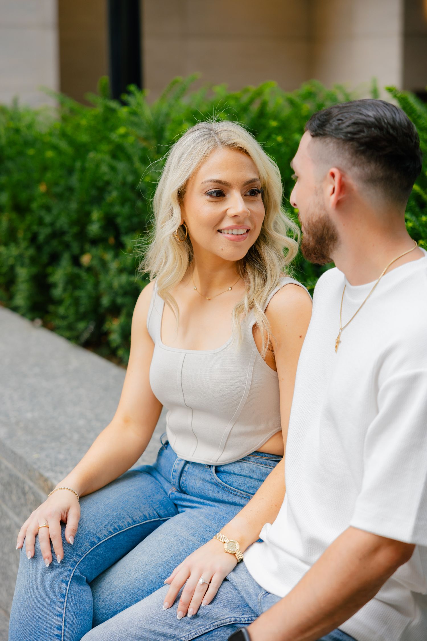A couple enjoying conversation while seated on outdoor steps near decorative shrubs.