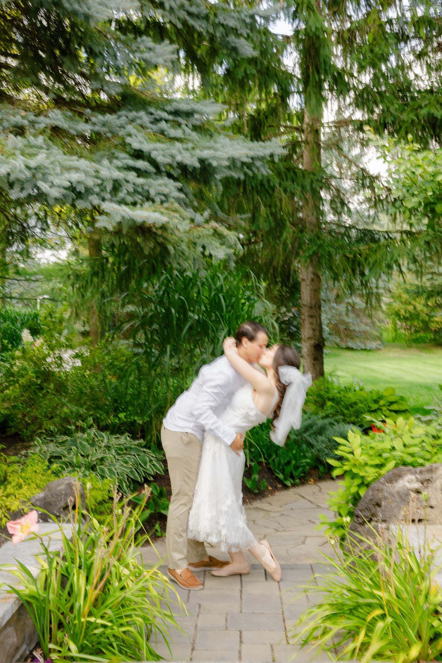 Wedding couple shares romantic dance move on garden pathway surrounded by flowers.