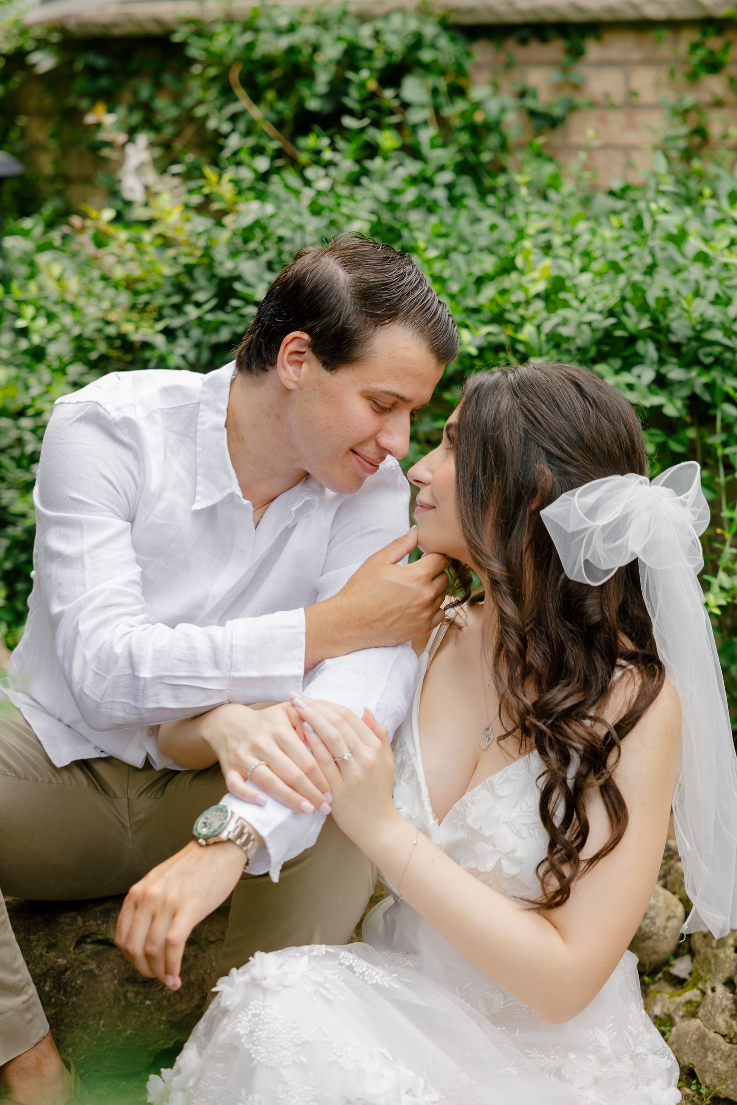 A romantic wedding couple shares an intimate moment surrounded by lush greenery in a garden setting.