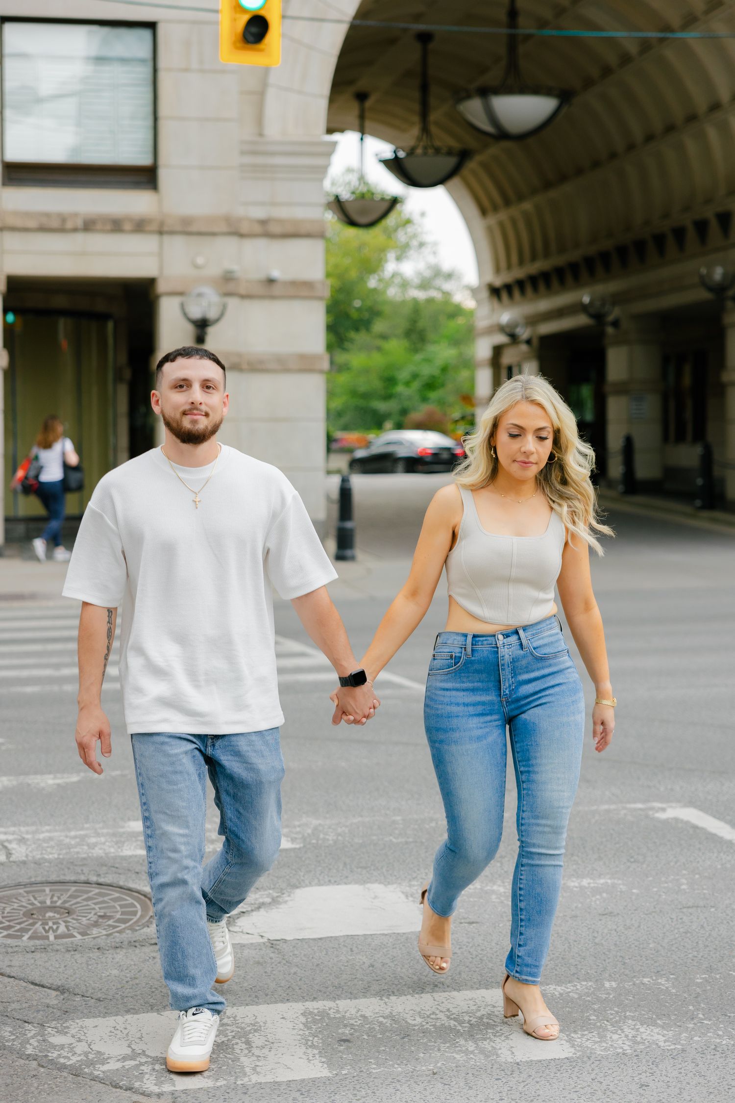 Couple holding hands while walking together on a city street wearing matching casual outfits.