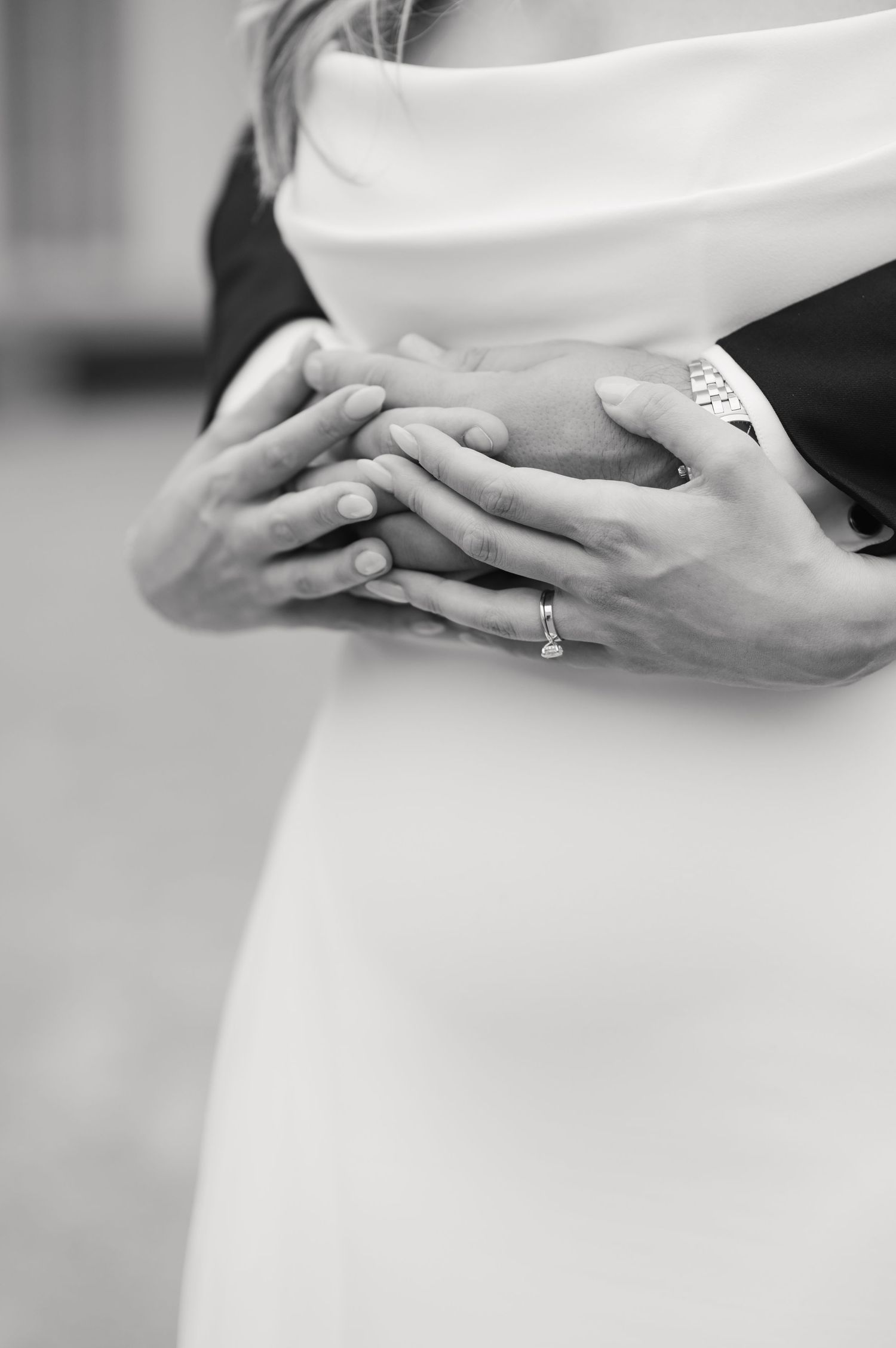 Close-up black and white photo of hands with wedding rings and white dress fabric.