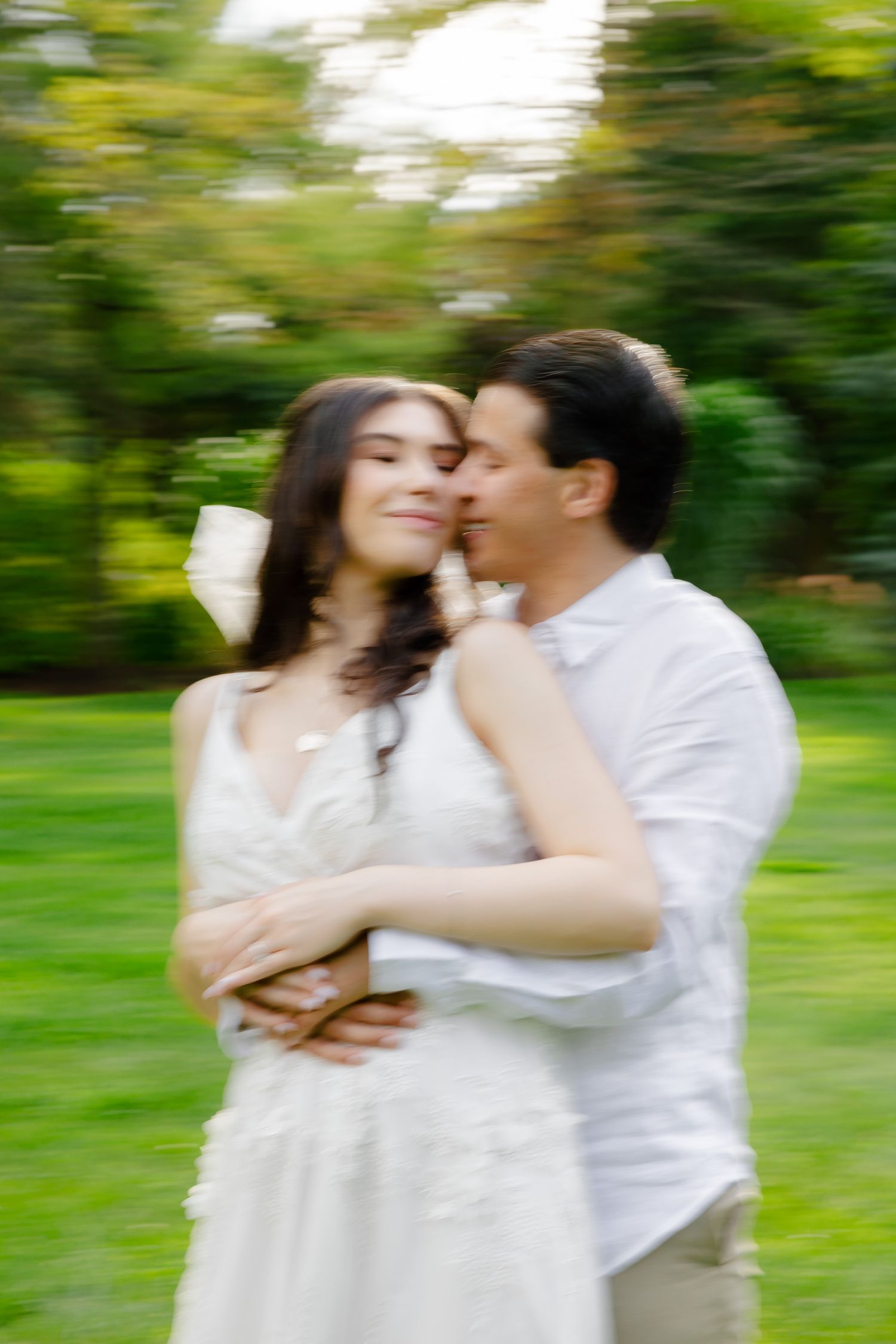 Dreamy soft-focus portrait of couple in white clothing sharing tender moment in park.
