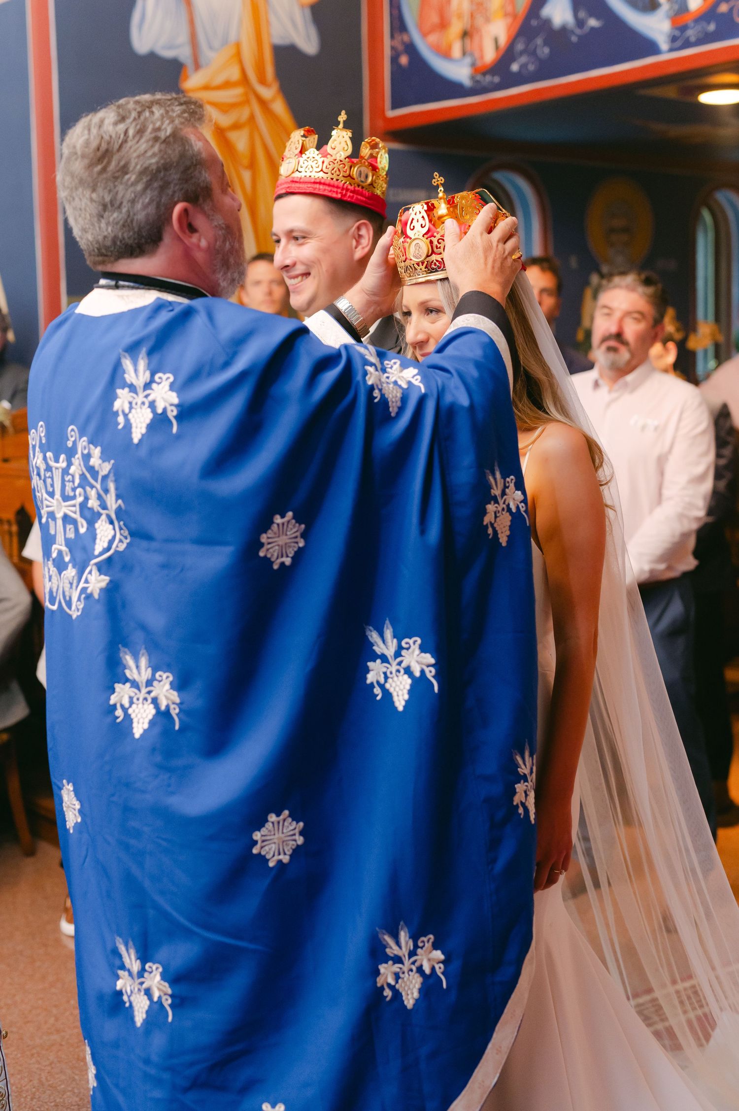 Orthodox priest in blue embroidered vestments performing traditional crown ceremony during wedding.