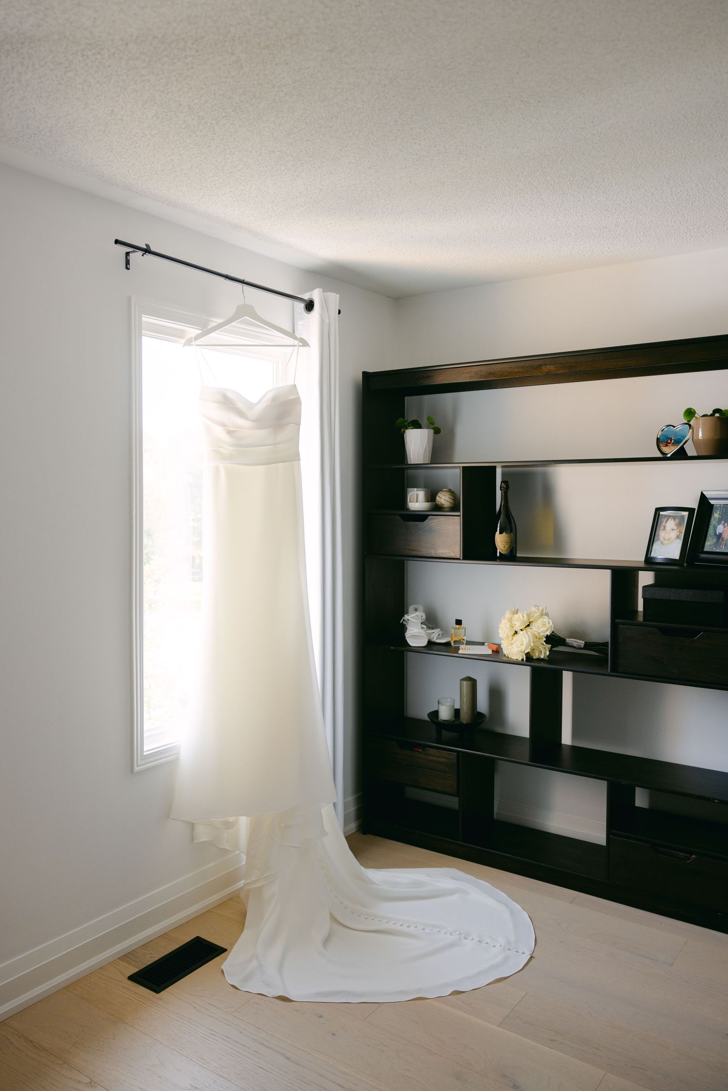 White wedding dress hanging in a modern room with dark shelving unit.